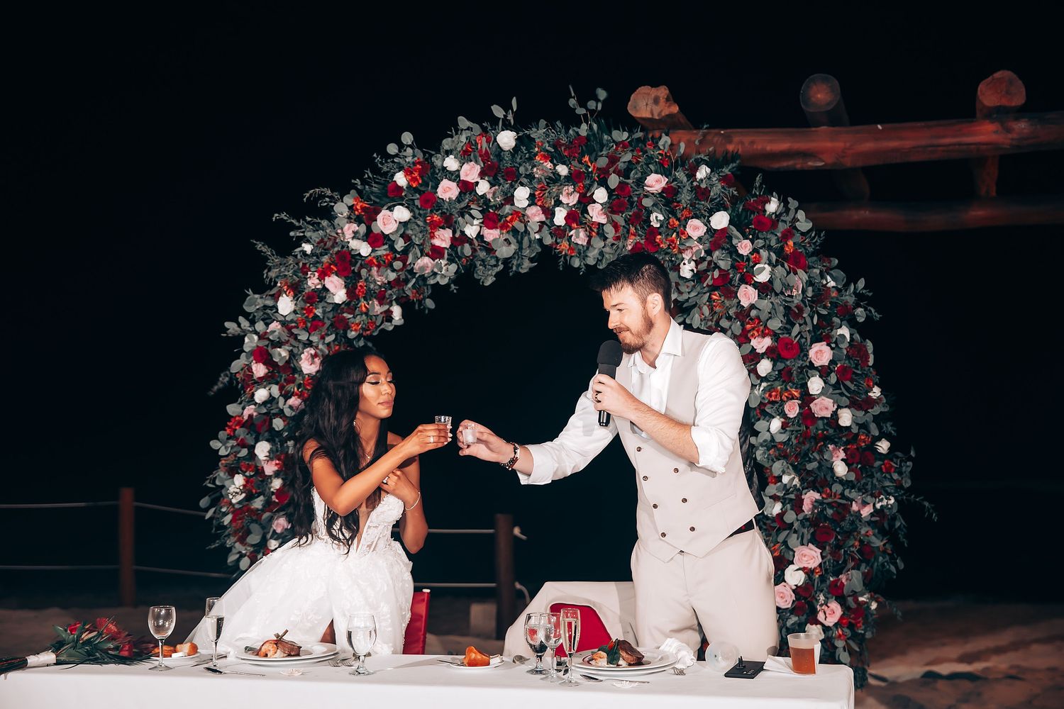 Wedding couple performs a dance routine in front of a floral arch during their reception celebration.