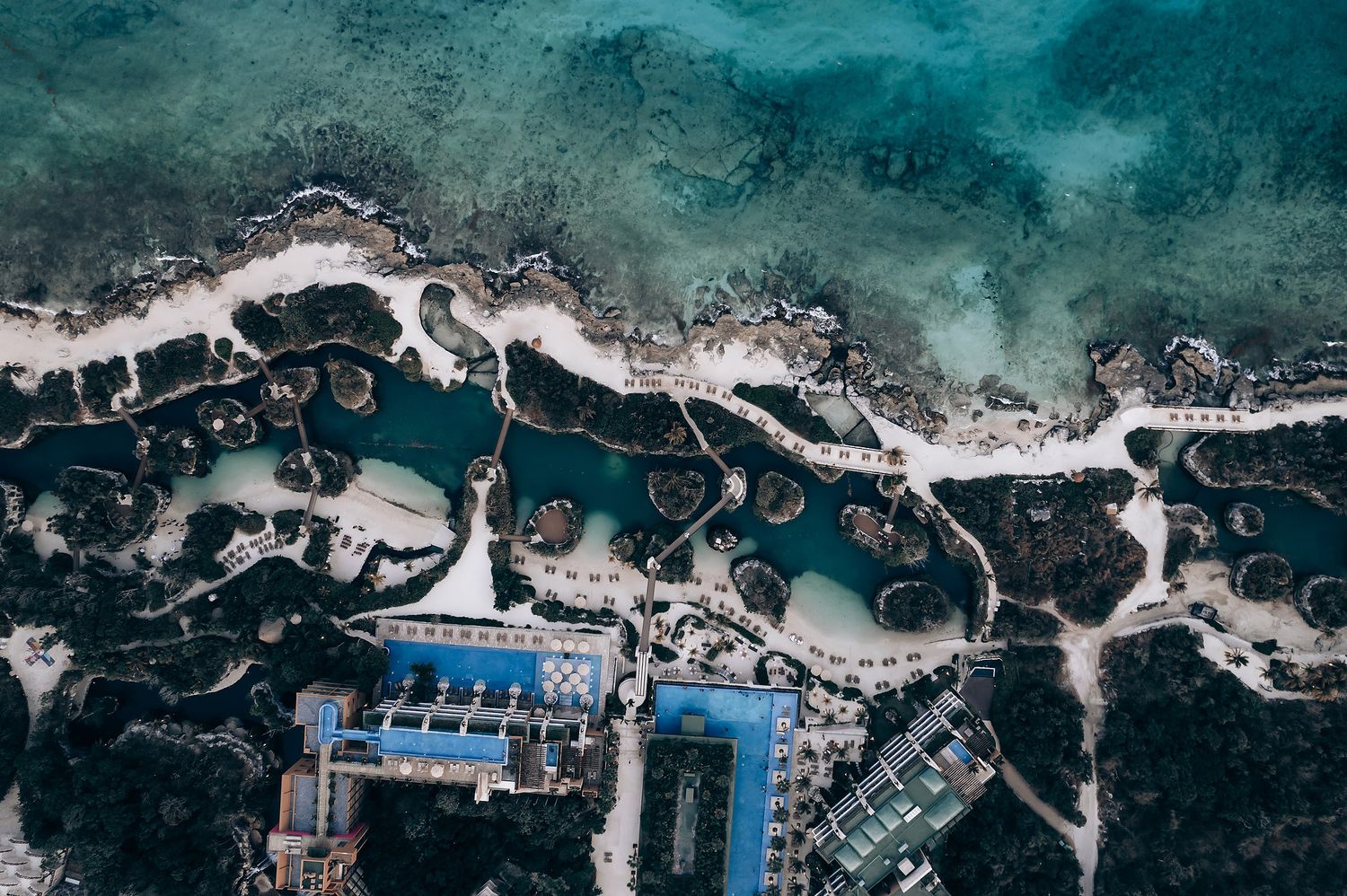Aerial view of a turquoise coastline with rocky formations and blue swimming pools.