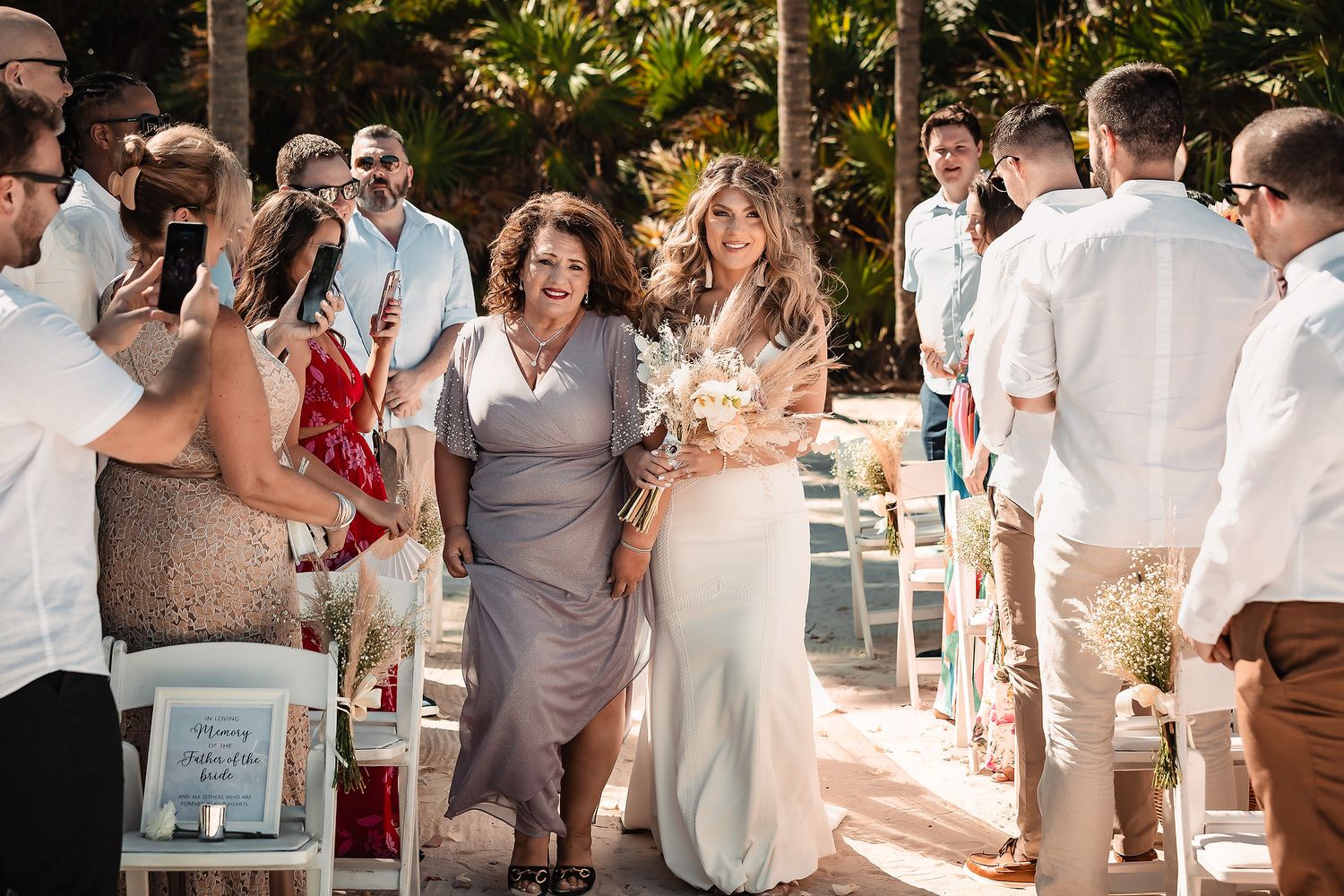 Wedding guests celebrate and dance during an outdoor beach reception in white and gray attire.