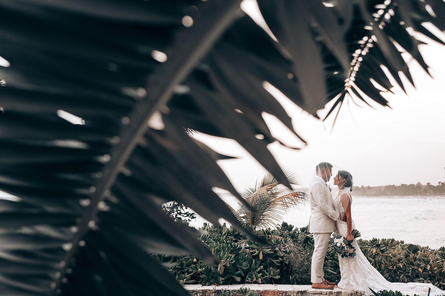 Romantic beach wedding ceremony setup with white chairs and floral arrangements at sunset.