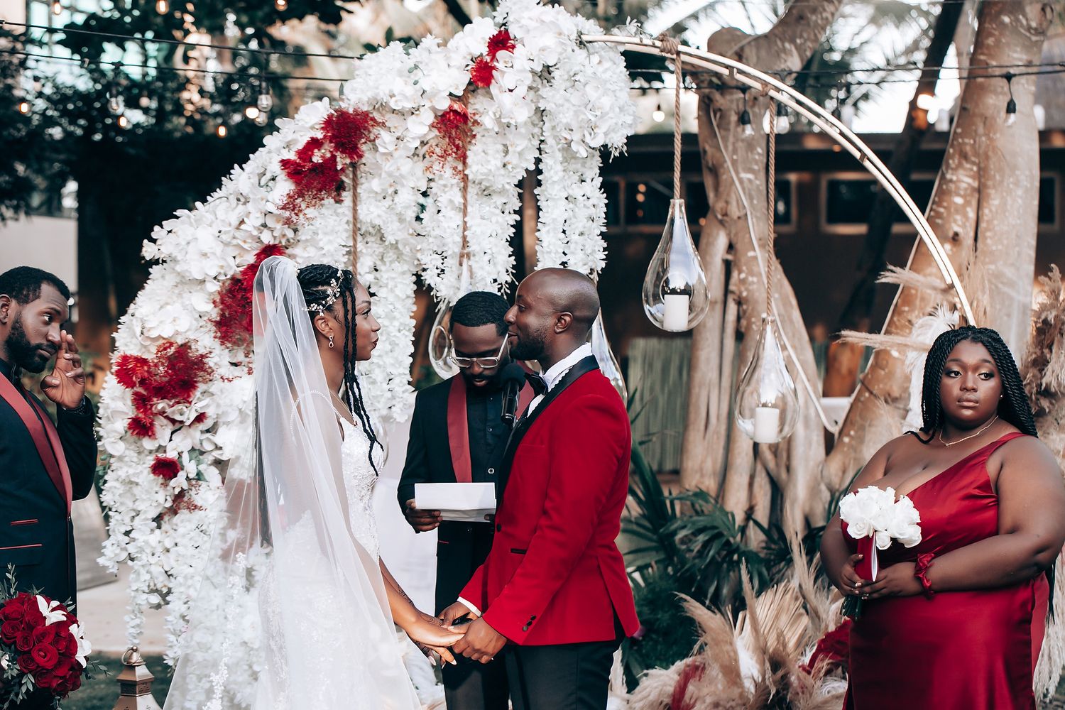 A wedding party poses together wearing red and white attire at an elegant indoor celebration.
