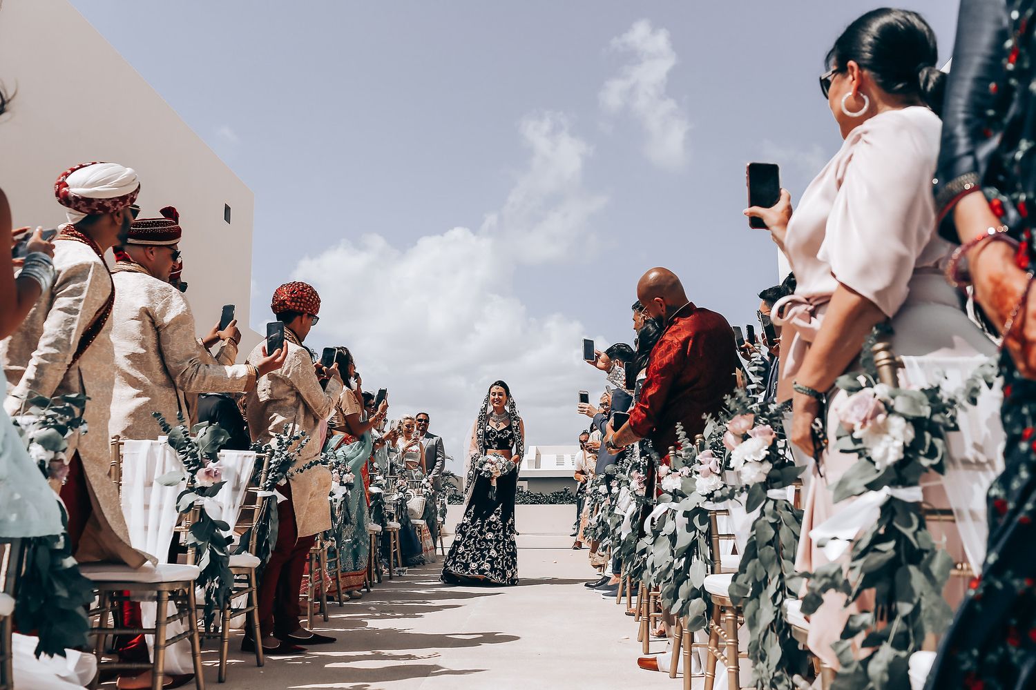 A group of people in camouflage uniforms dance in formation at an outdoor event under a bright sky.