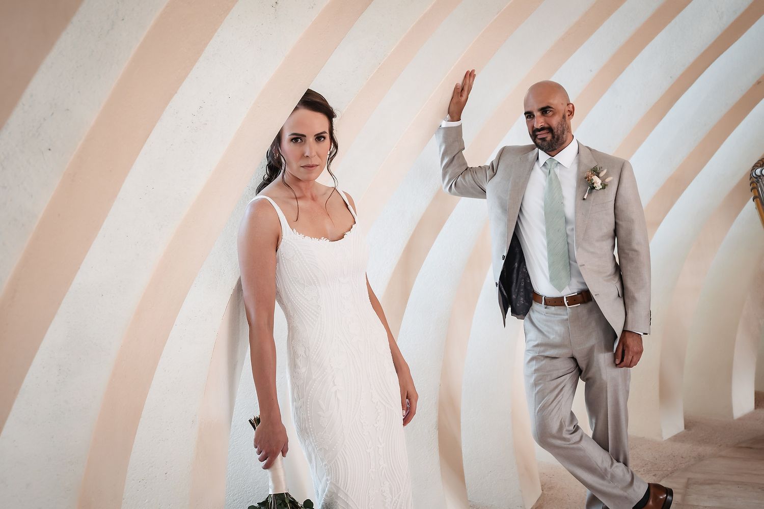A bride and groom pose playfully against a geometric striped wall in a modern setting.