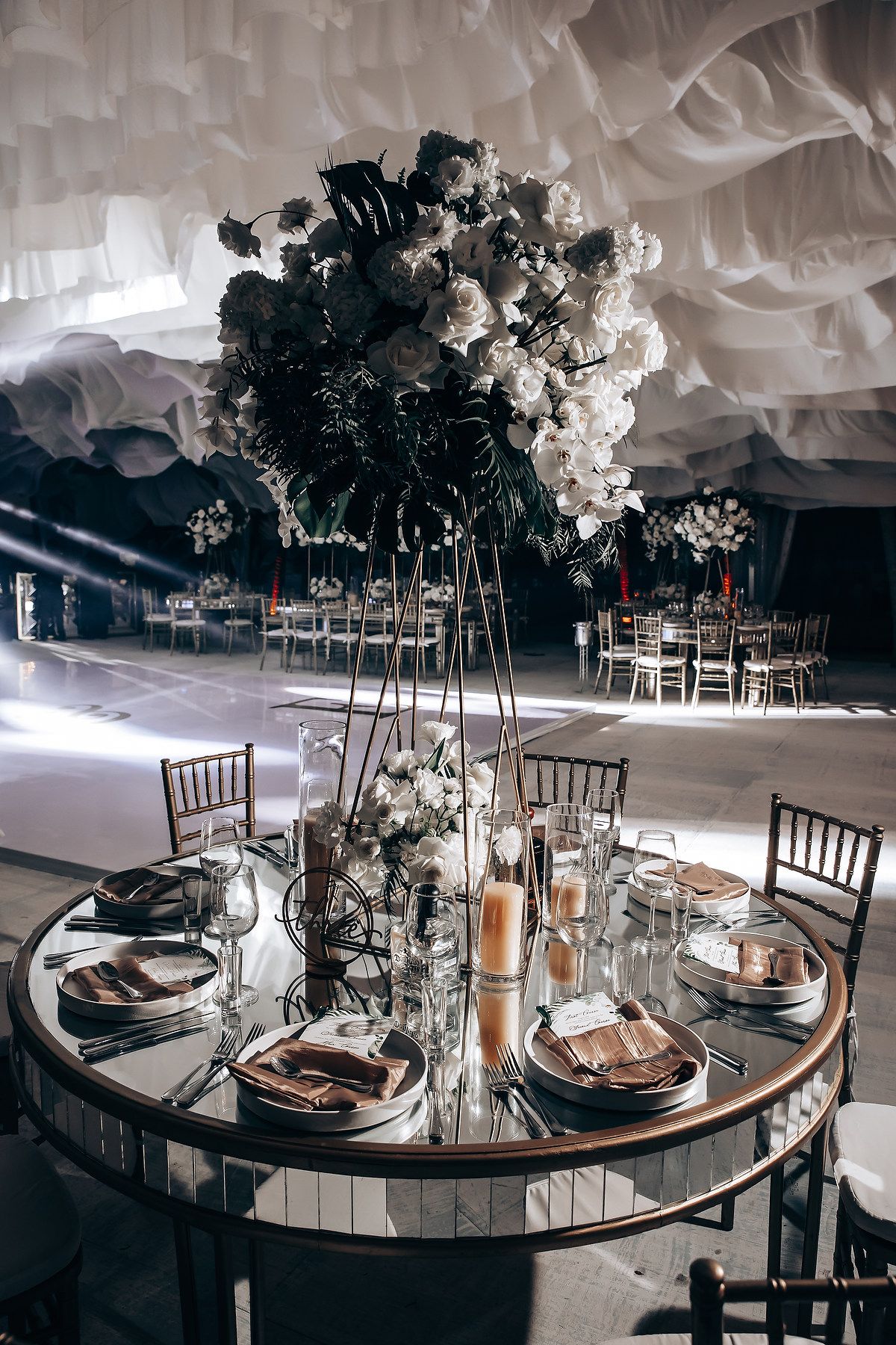 Dramatic wedding reception setup with tall floral centerpiece and mirrored round table.