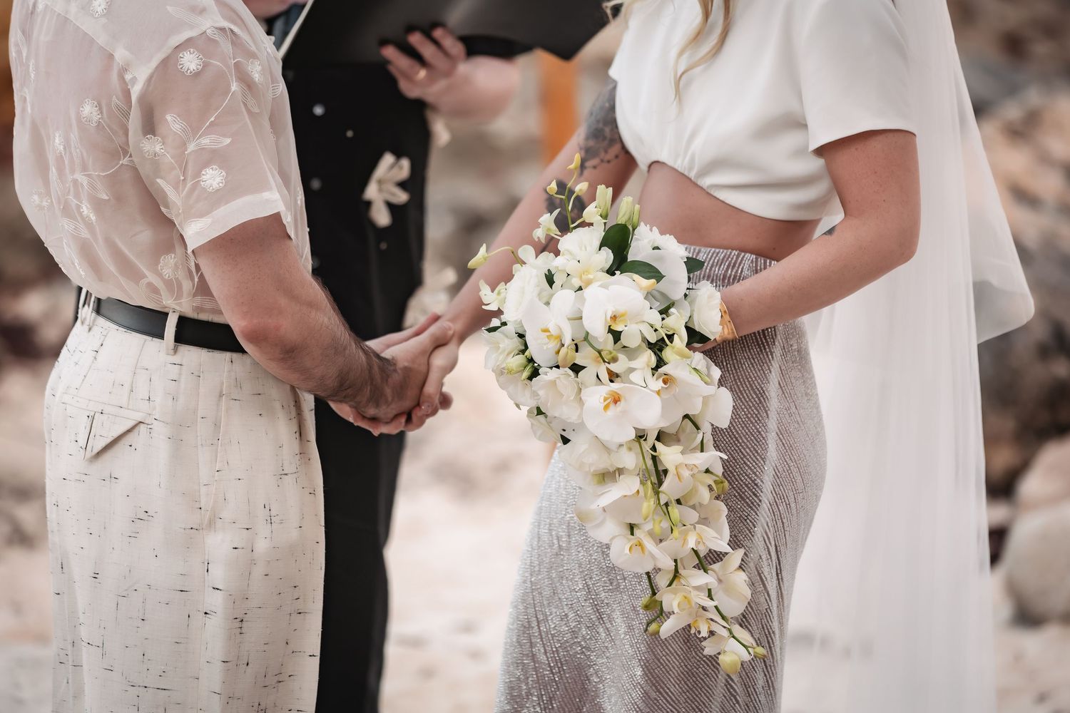 Wedding ceremony close-up showing white floral bouquet and formal attire.