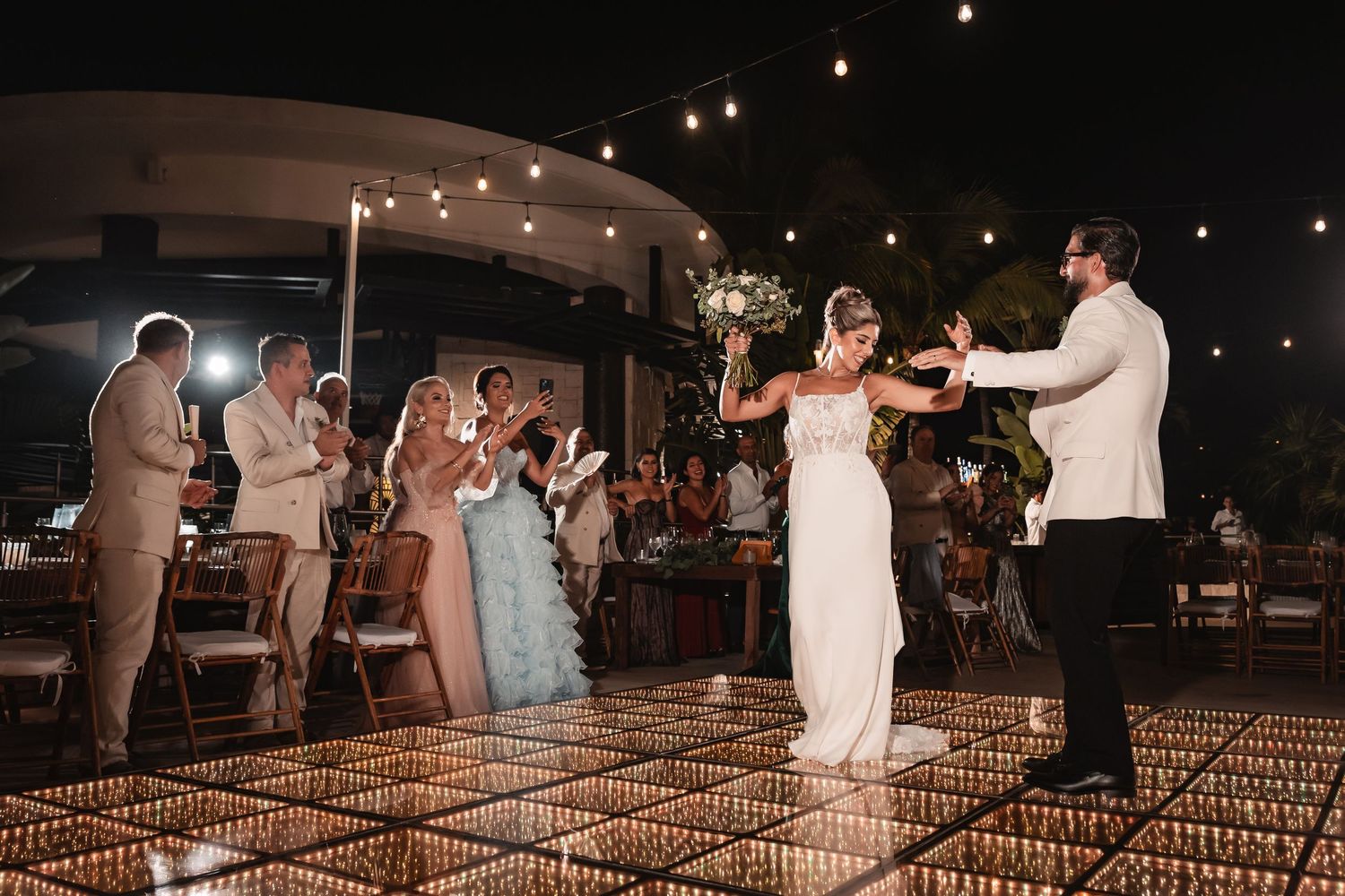 Wedding guests celebrate as the couple shares their first dance on an illuminated dance floor.