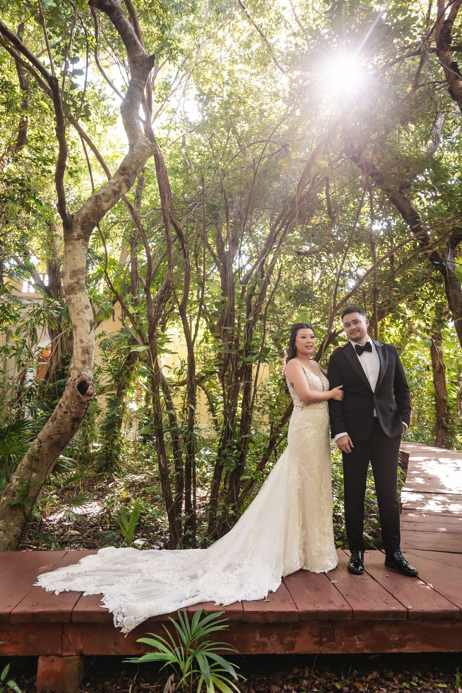 Sunlit wedding portraits on a wooden deck with natural forest backdrop.