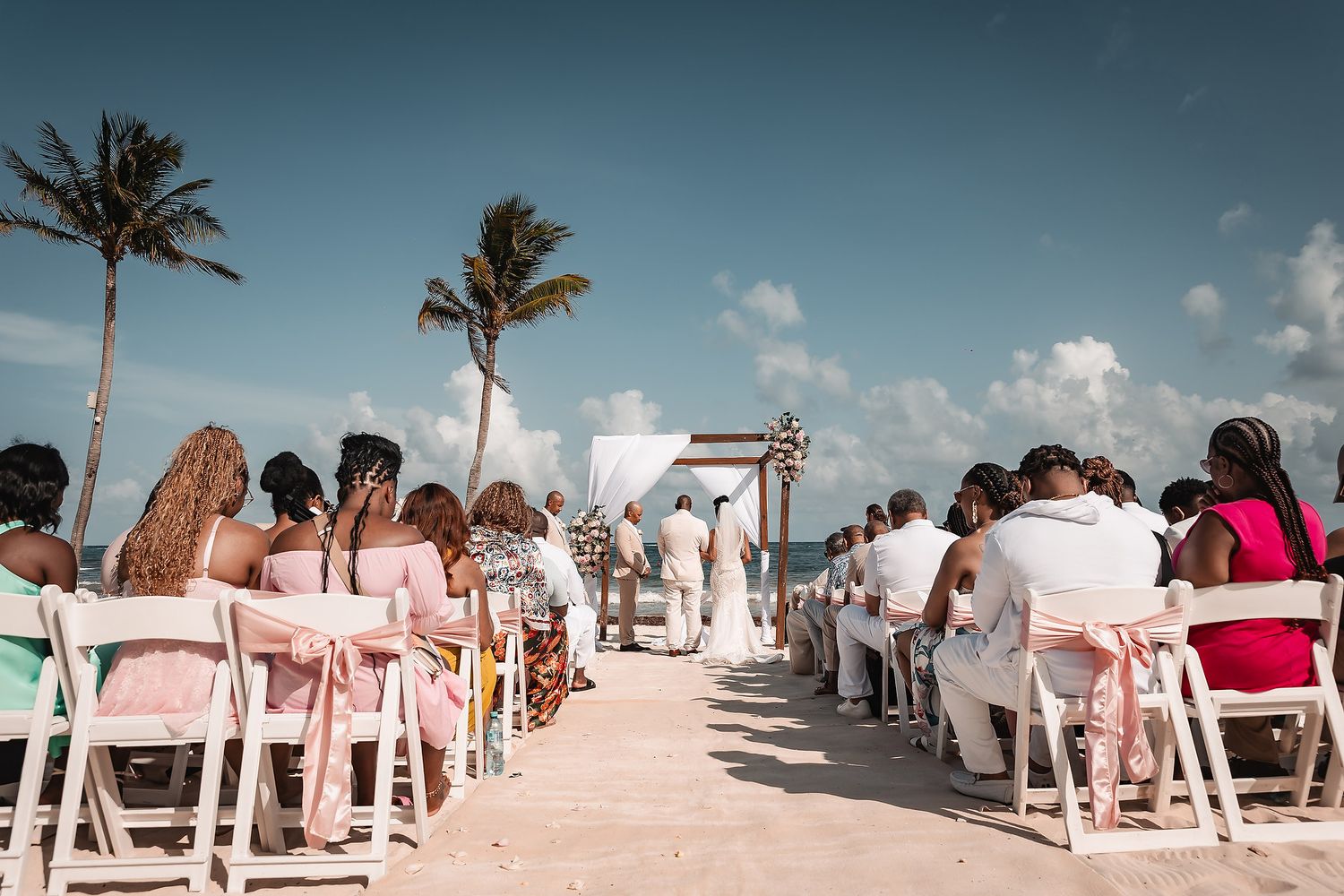Wide angle view of beach wedding ceremony with guests seated on white chairs.