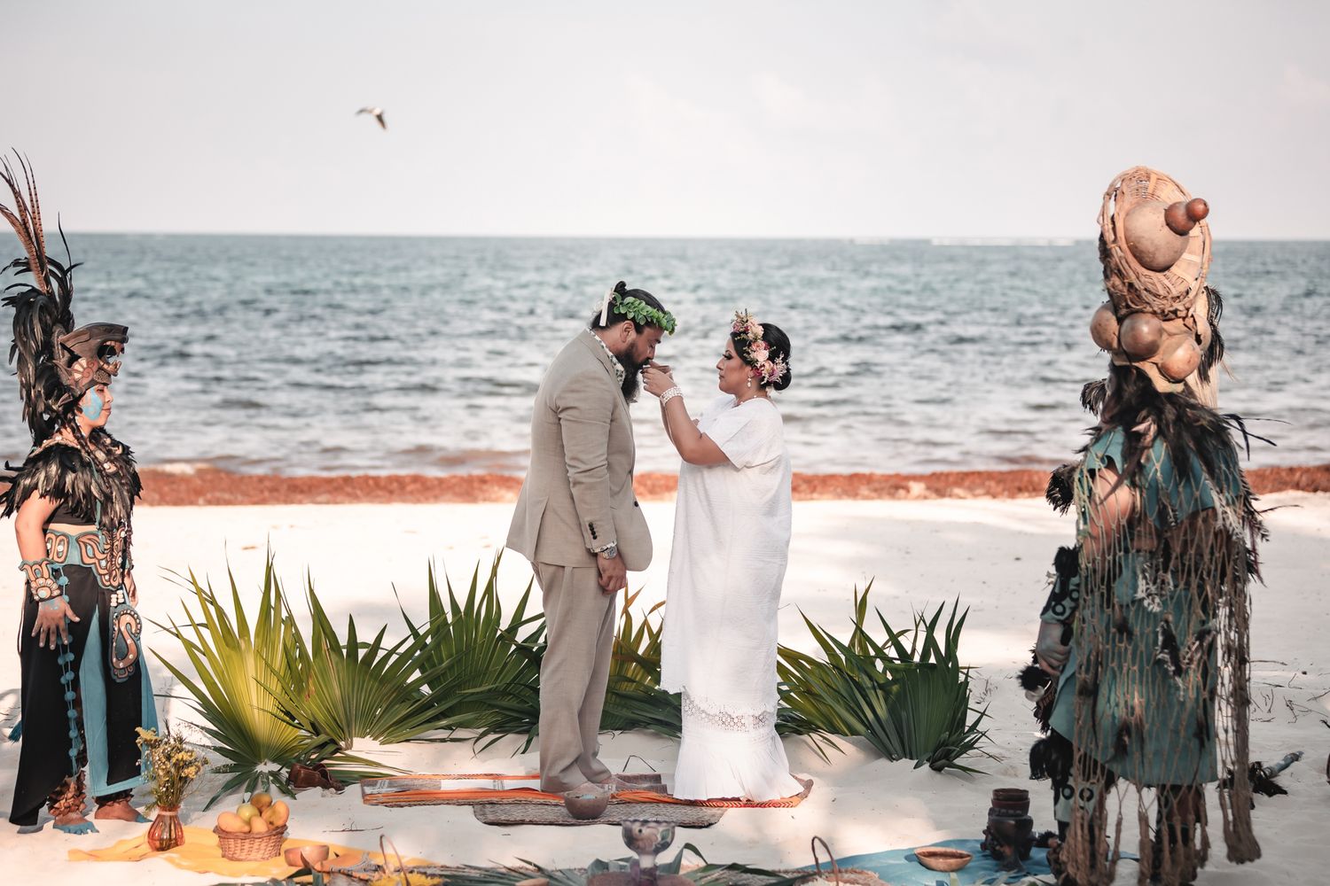 Couple exchanges vows on a beach wedding ceremony with Mayan performers and ocean backdrop.