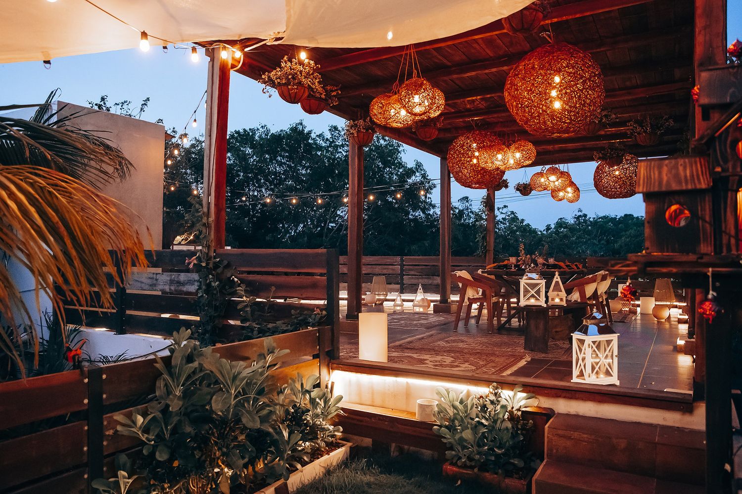 Elegant open-air restaurant patio at twilight featuring rattan hanging lamps and candlelit dining tables.