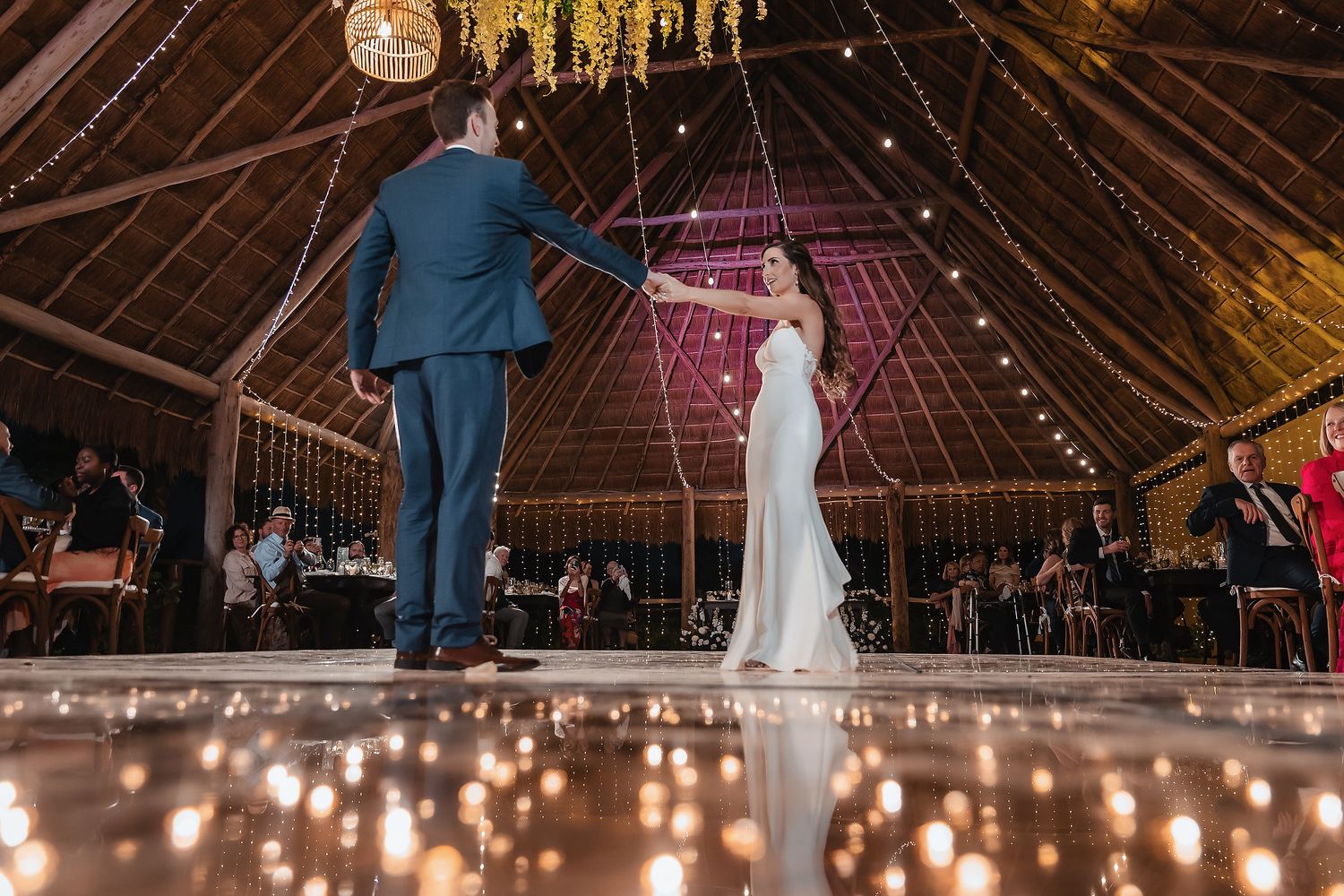 Bride and groom share their first dance on a candlelit floor inside a rustic barn wedding venue.