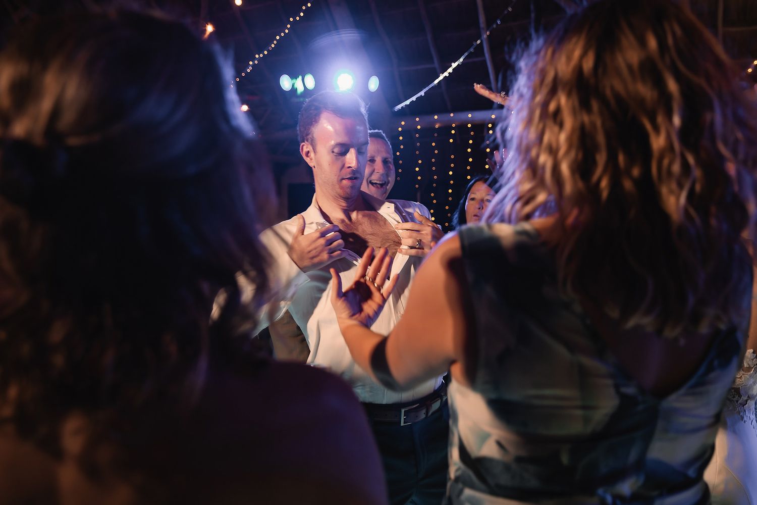 Guests dancing and socializing at an elegant indoor wedding reception with string lights in the background.
