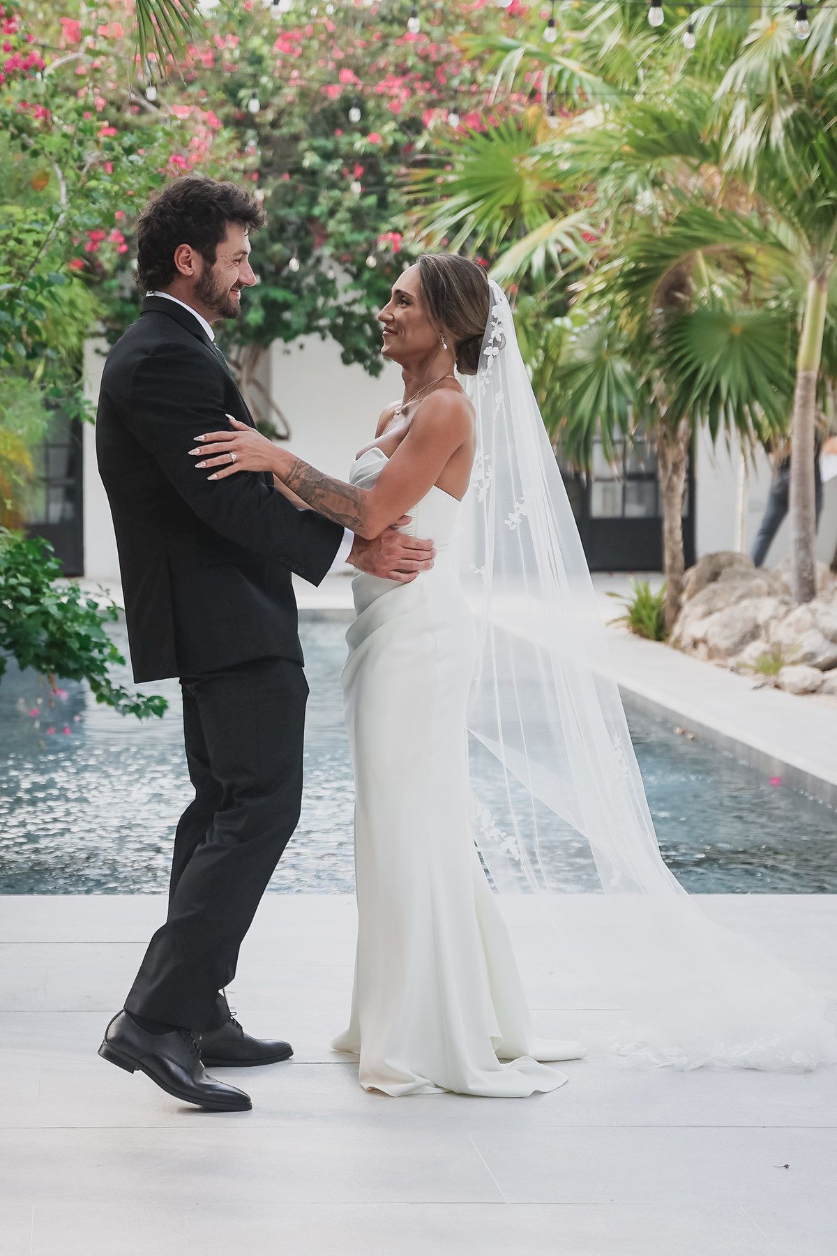 Bride and groom share romantic first look by tropical pool in elegant wedding attire.