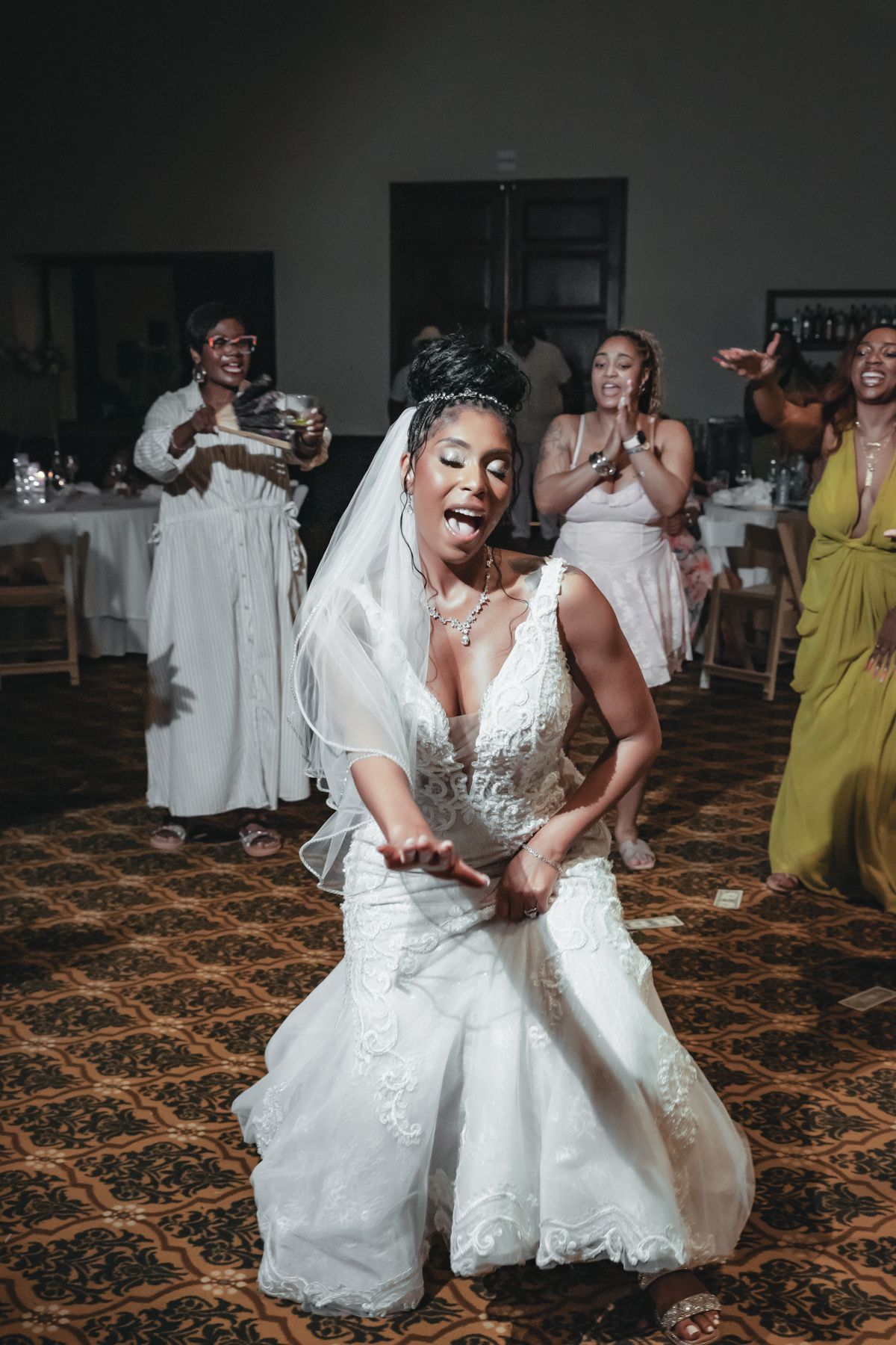 A joyful bride in a white lace wedding gown and veil dances energetically at her wedding reception.