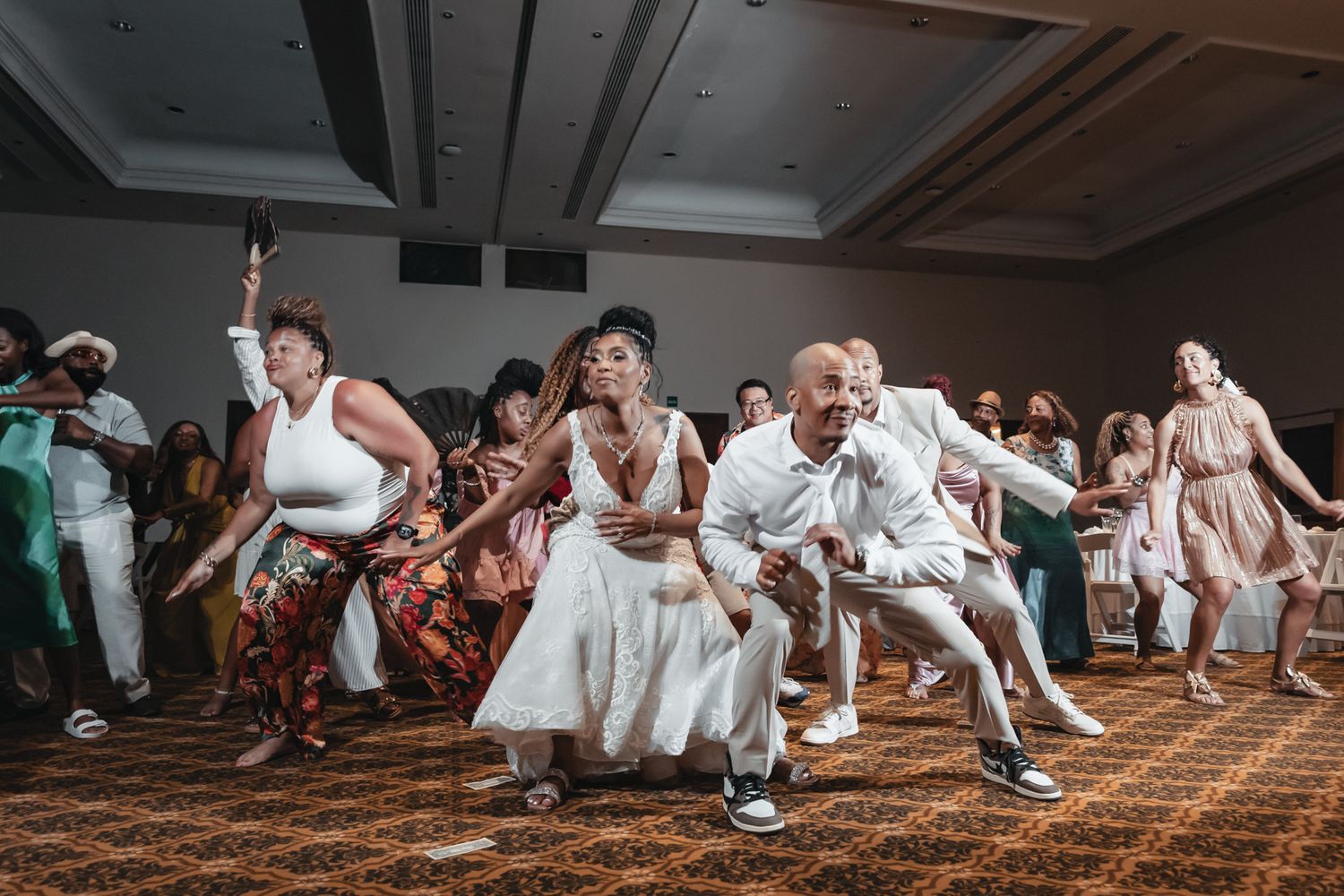Wedding guests energetically dancing together in a ballroom during a lively reception celebration.