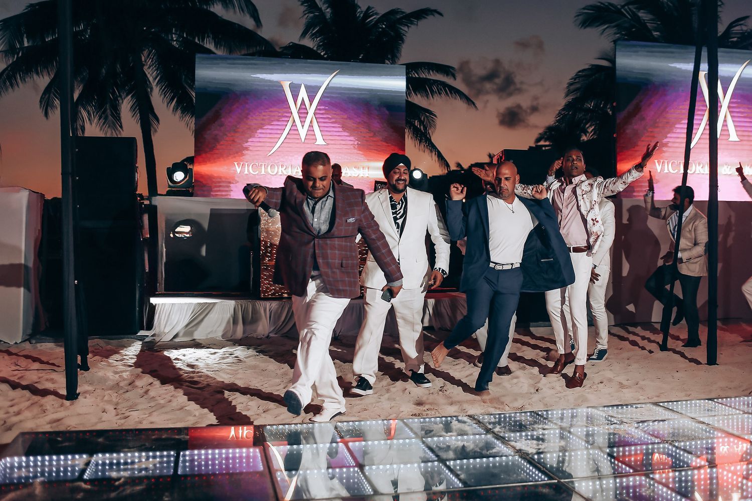 A group of people dancing and celebrating at a poolside party with palm trees and neon lights in the background.