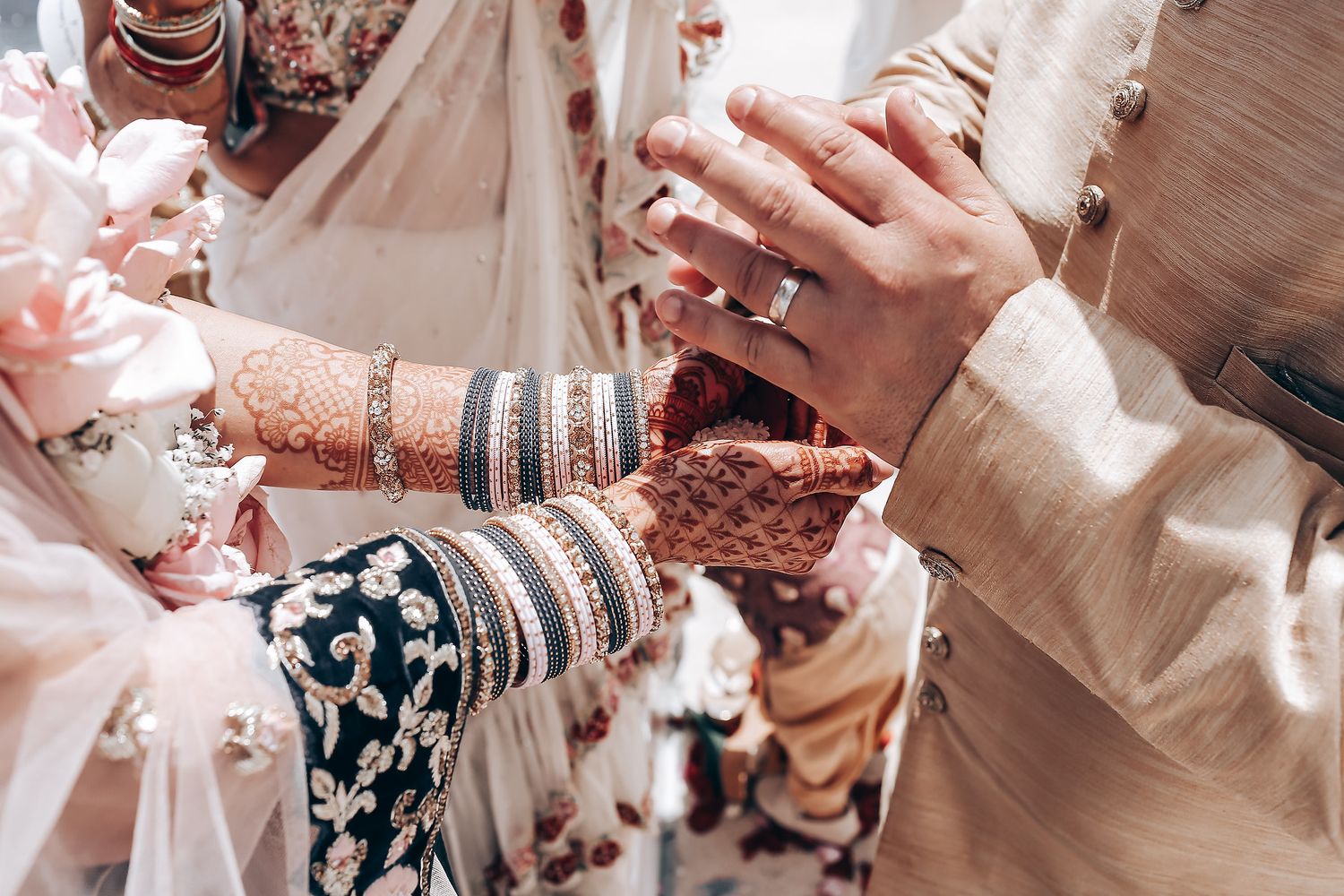 Hands adorned with traditional henna designs and bangles hold each other in celebration.
