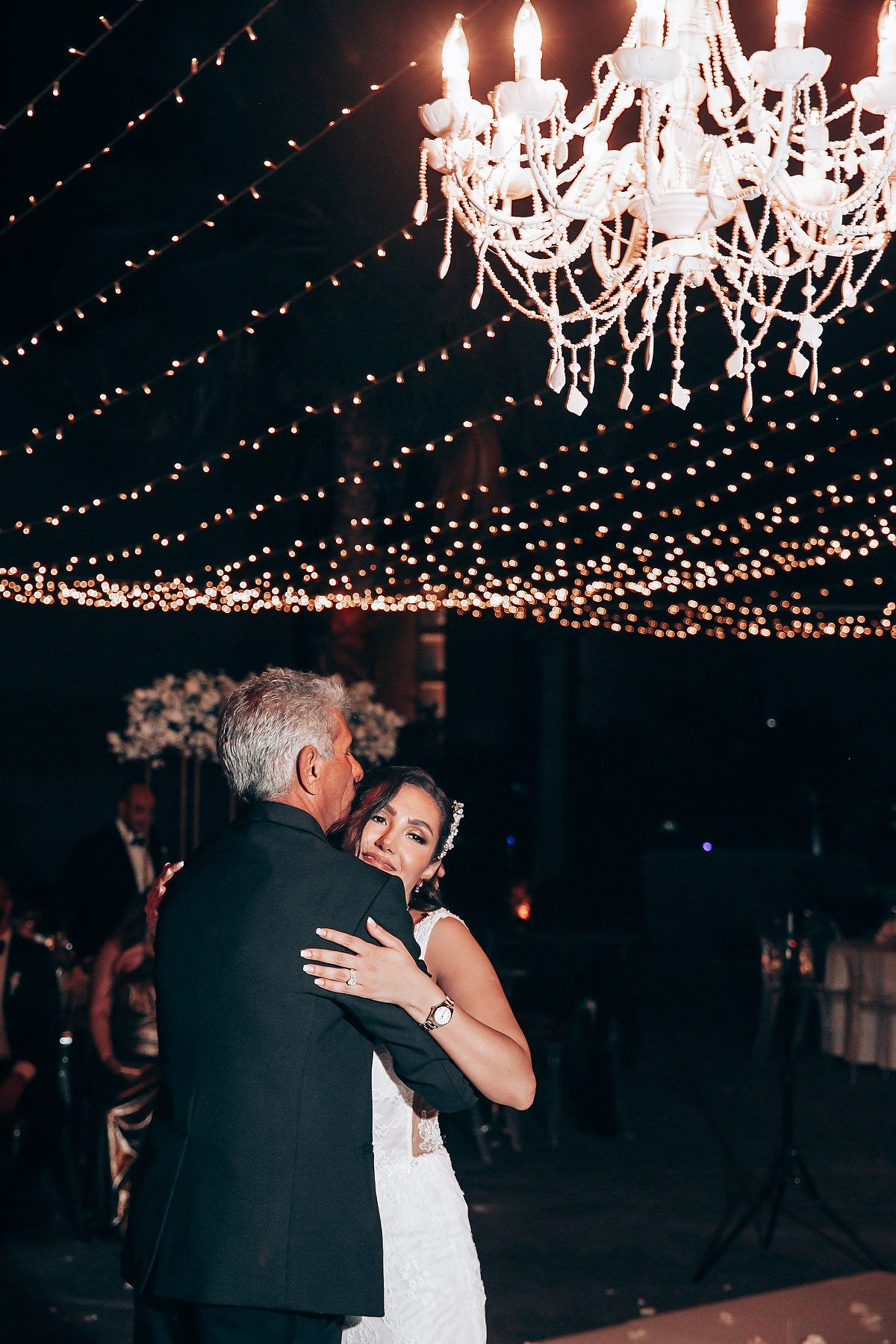 Intimate dance under crystal chandeliers and string lights at an elegant evening wedding reception.