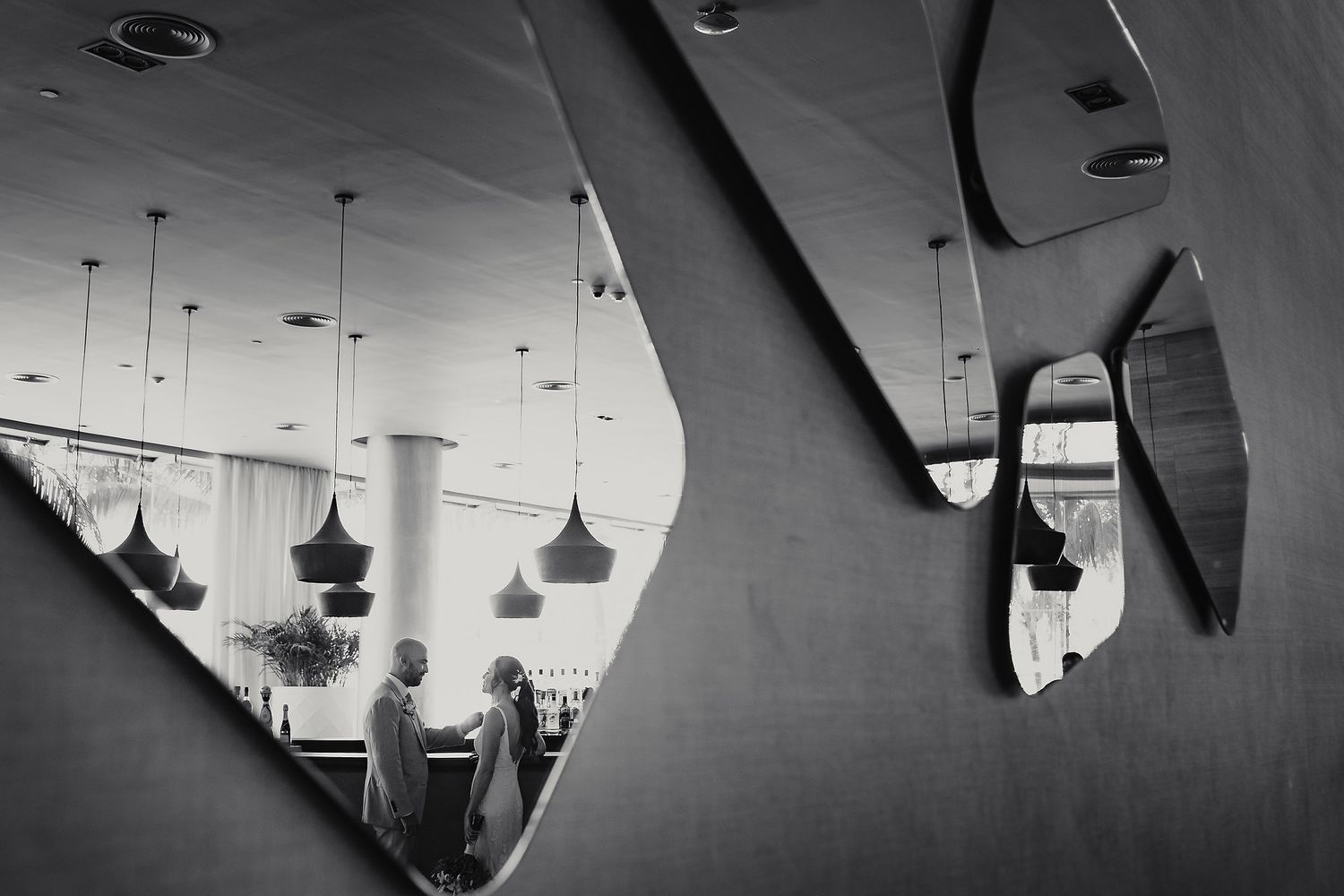 Abstract black and white reflection through a geometric mirror showing pendant lights and silhouettes.