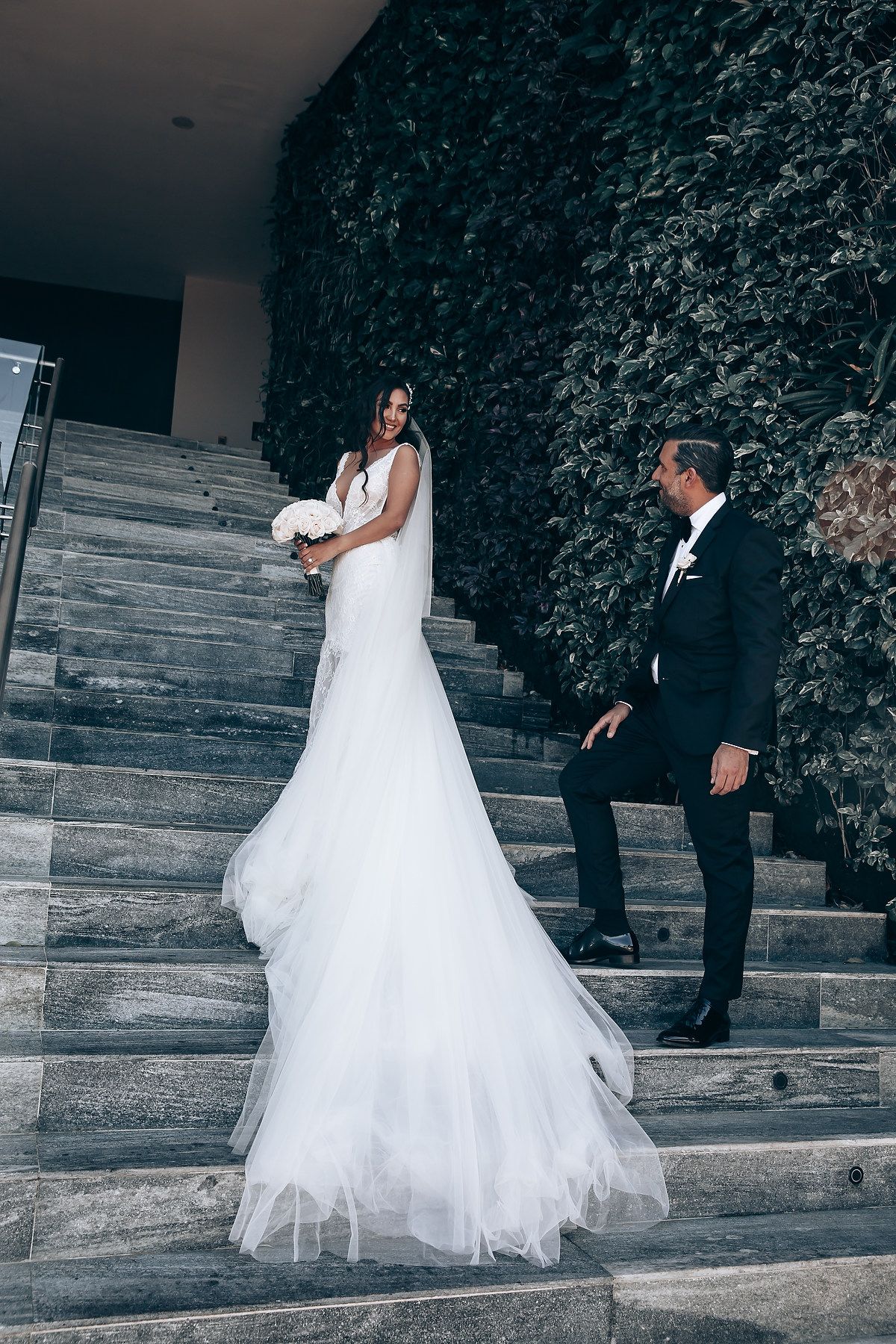 A wedding couple descends elegant stone steps surrounded by lush greenery in a series of romantic moments.