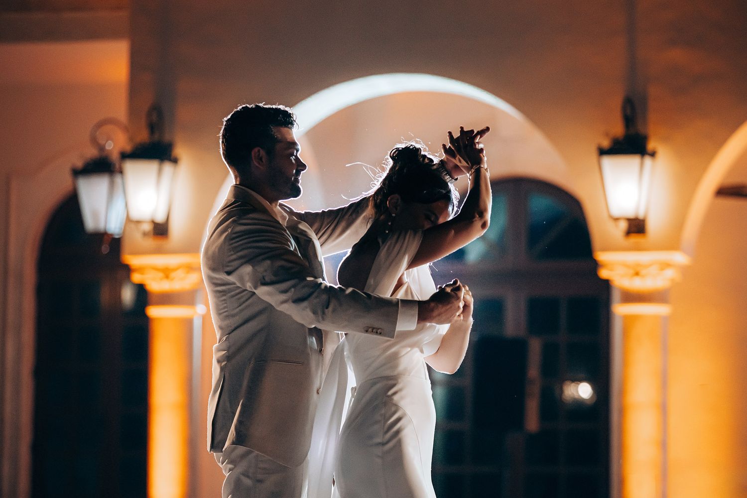 A couple shares their first dance at a romantic evening wedding reception under illuminated archways and lanterns.