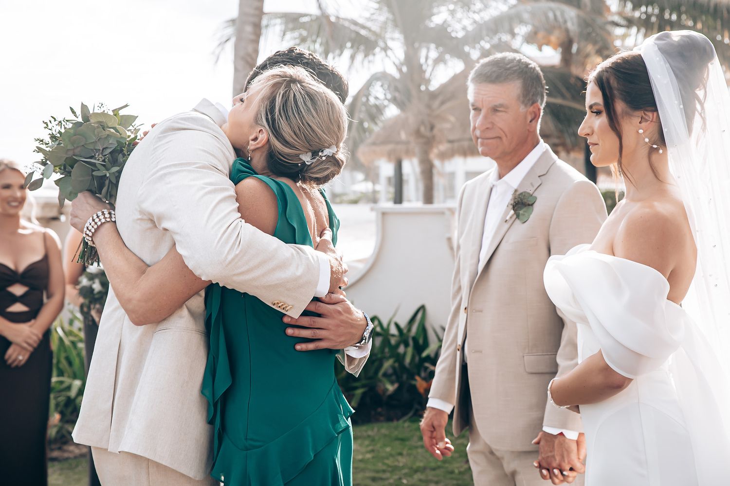 Wedding guests share joyful moments during an outdoor celebration in a tropical garden setting with palm trees.