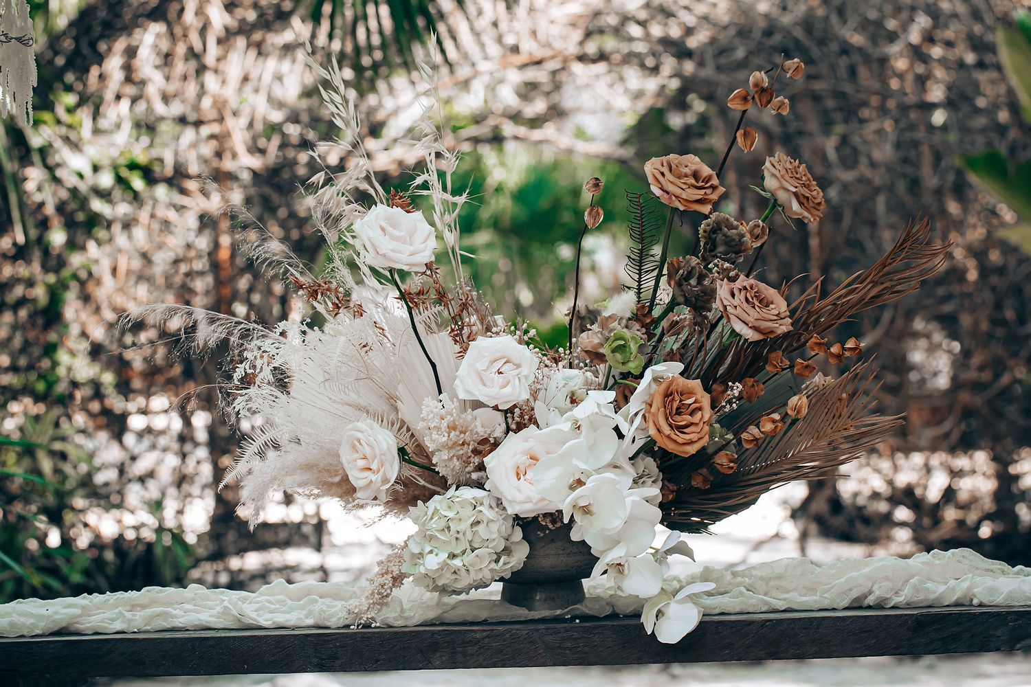 Elegant floral arrangement featuring dried white flowers and brown roses on a rustic surface.