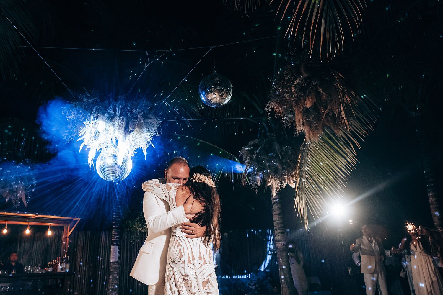 A couple shares a romantic dance under twinkling lights at an outdoor evening wedding reception.