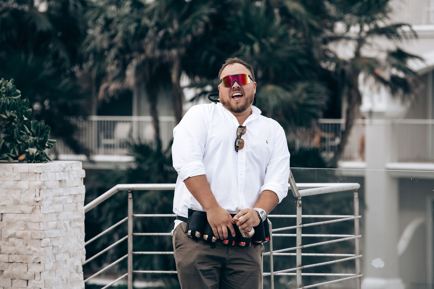 A stylishly dressed person in white shirt and sunglasses poses on an outdoor balcony.