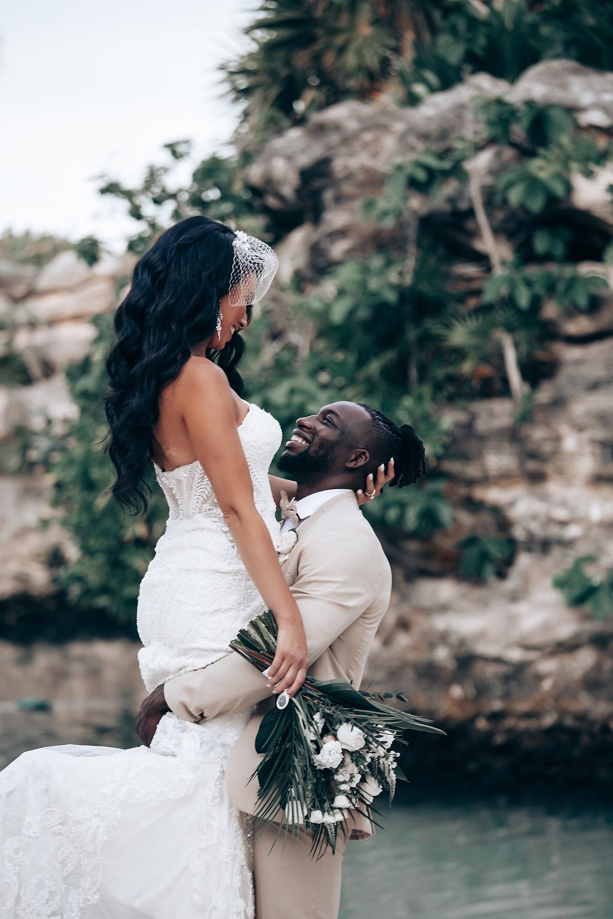 Intimate wedding couple moment captured against a rocky tropical backdrop near water.