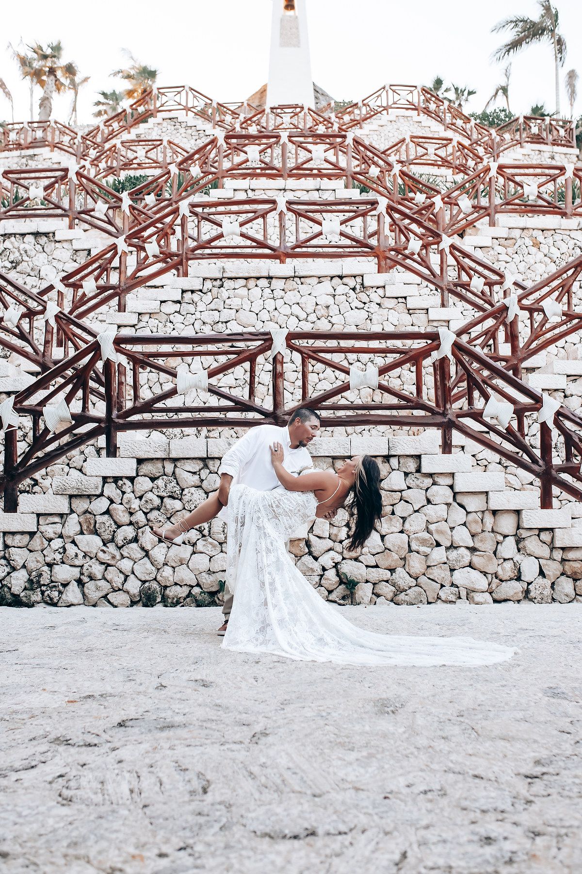 Wedding couple takes romantic photos along rustic wooden bridge and stone wall at beach.