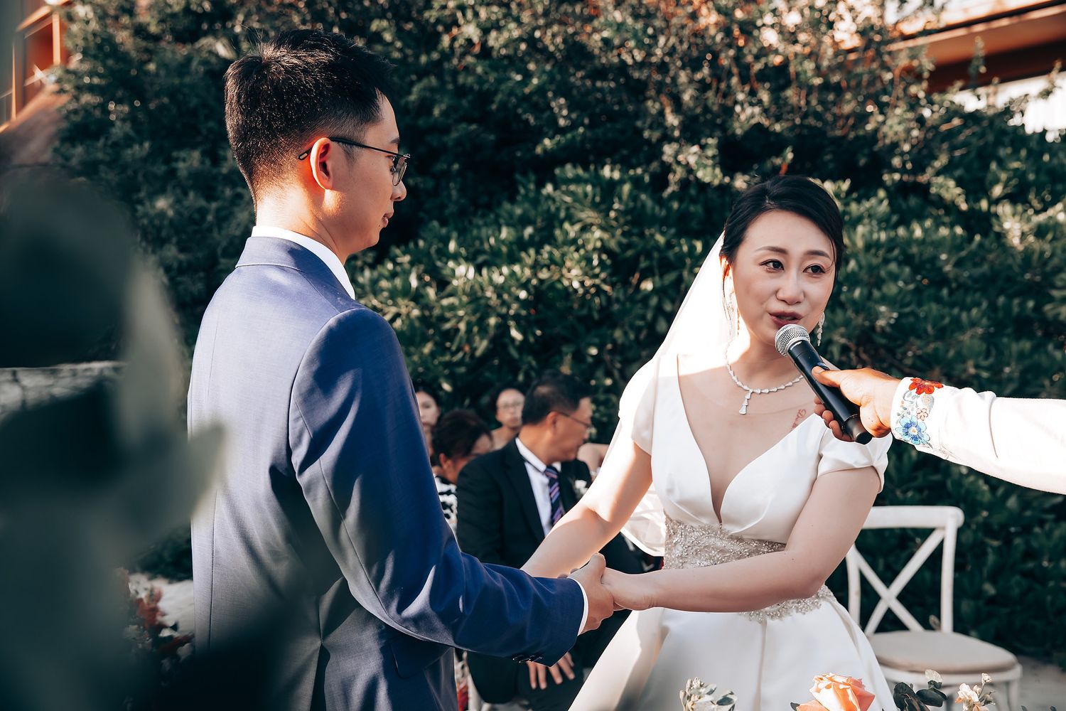 Outdoor wedding ceremony with couple speaking into microphones during their vows.