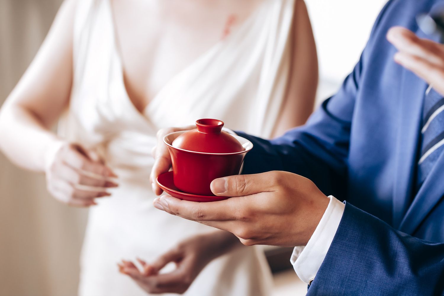 Hands holding a traditional red Chinese tea ceremony cup during a wedding celebration.