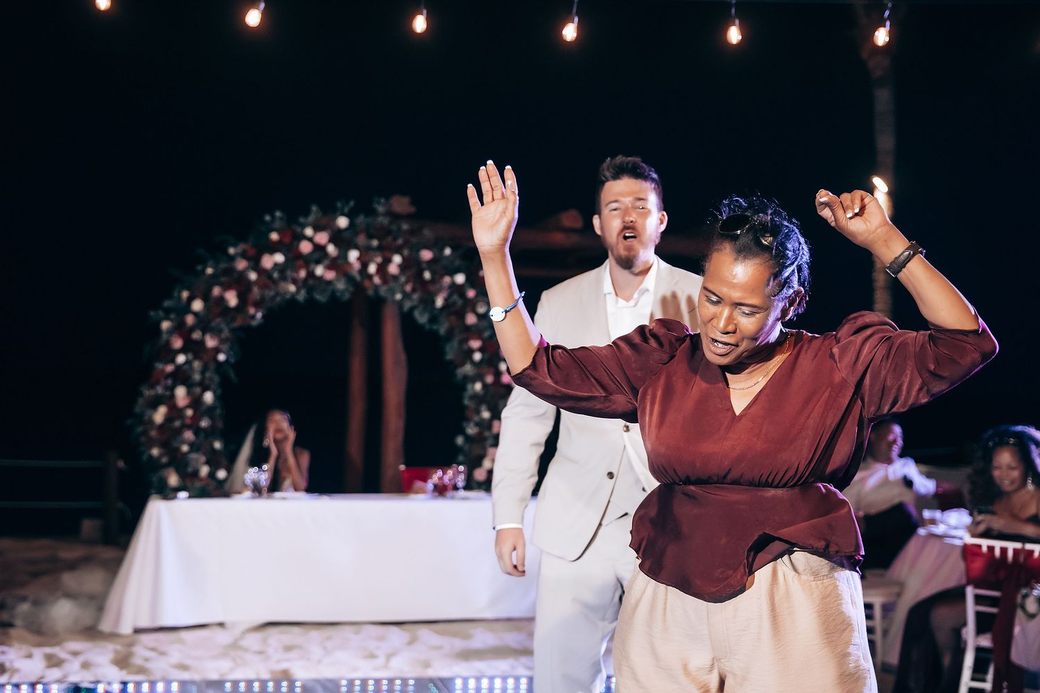 Wedding guests dancing and celebrating under string lights at outdoor evening reception.