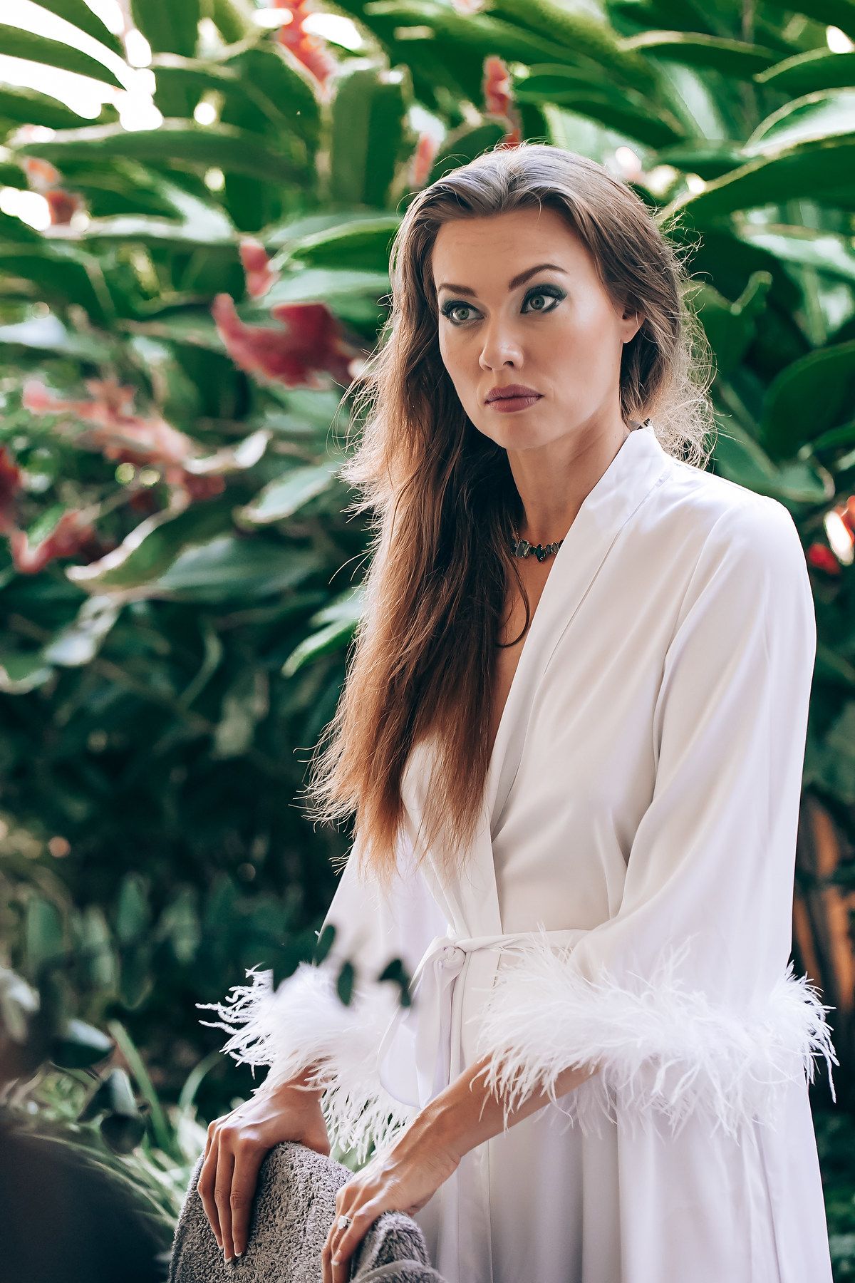 White feather-trimmed robe photographed against tropical foliage background.