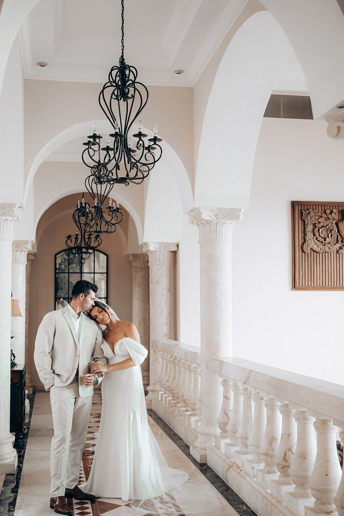Elegant white corridor with arches and chandeliers featuring wedding moment.
