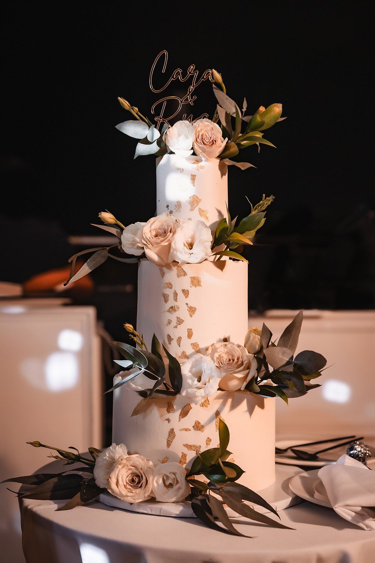 Elegant white wedding cake decorated with delicate roses and gold accents on display.