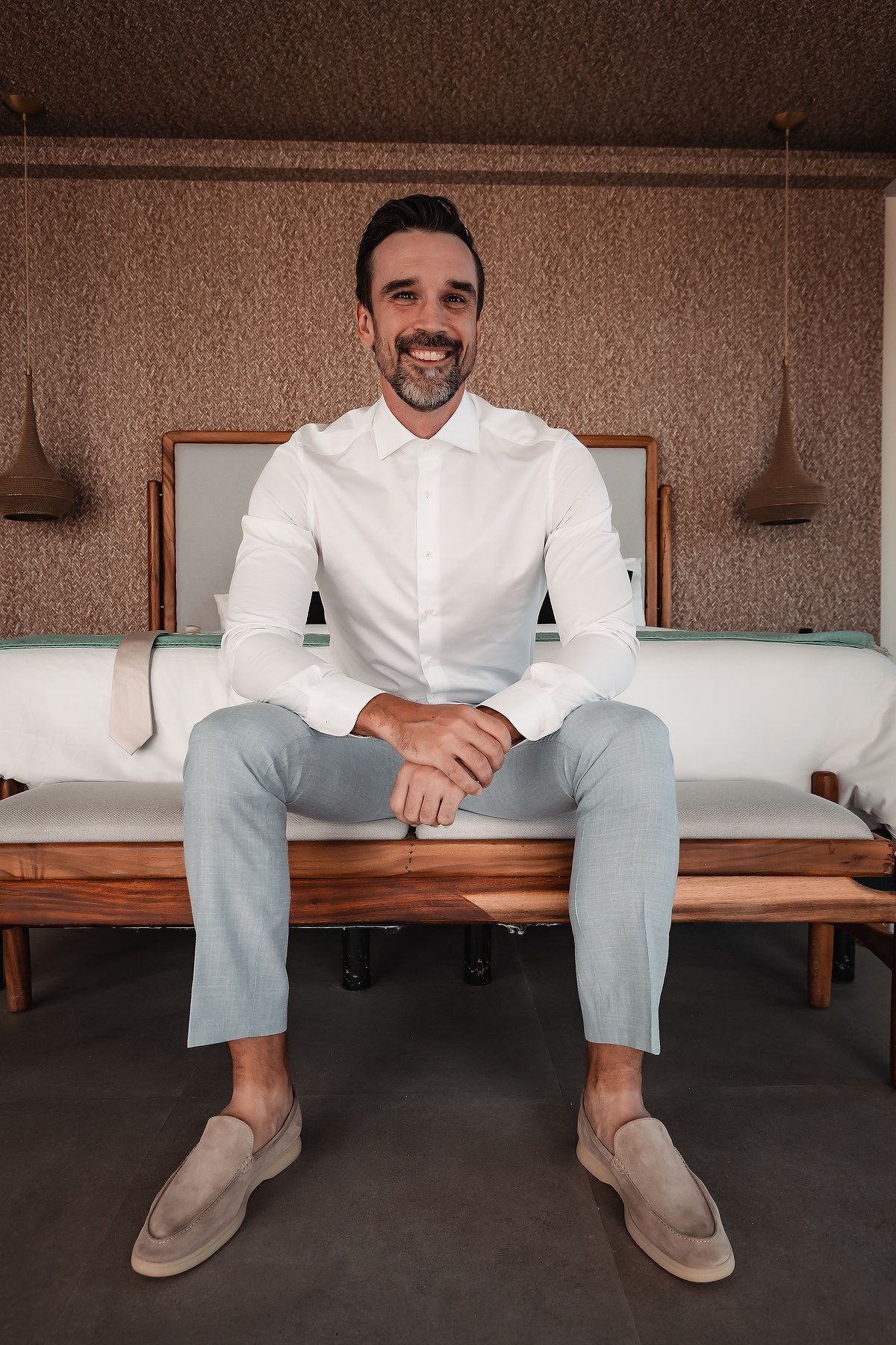 Man in white shirt and gray pants sitting casually on wooden bench.