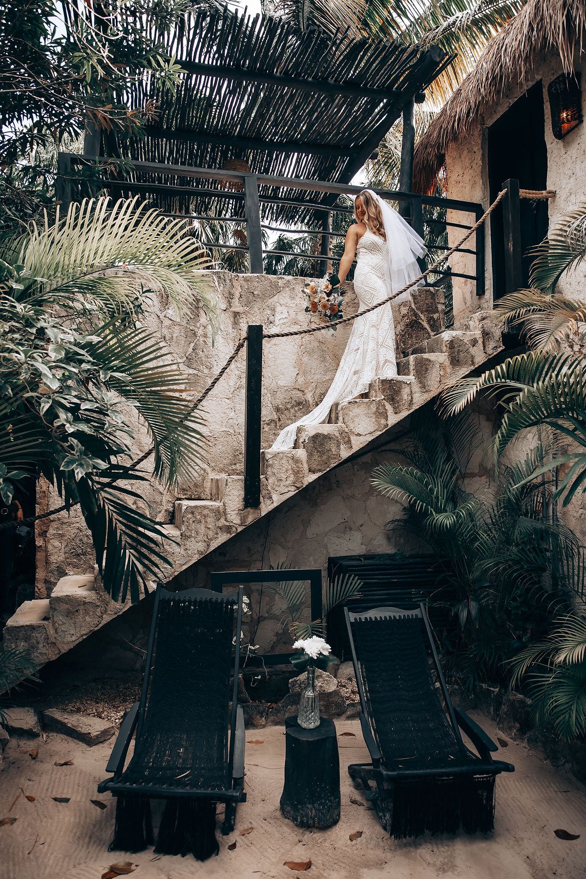 Wedding photos taken on stone steps surrounded by tropical palm plants and natural decor.