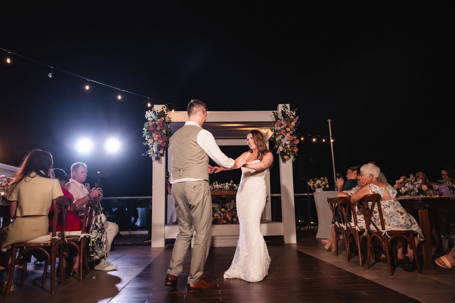 Wedding reception dance floor filled with guests under twinkling lights during evening celebration.