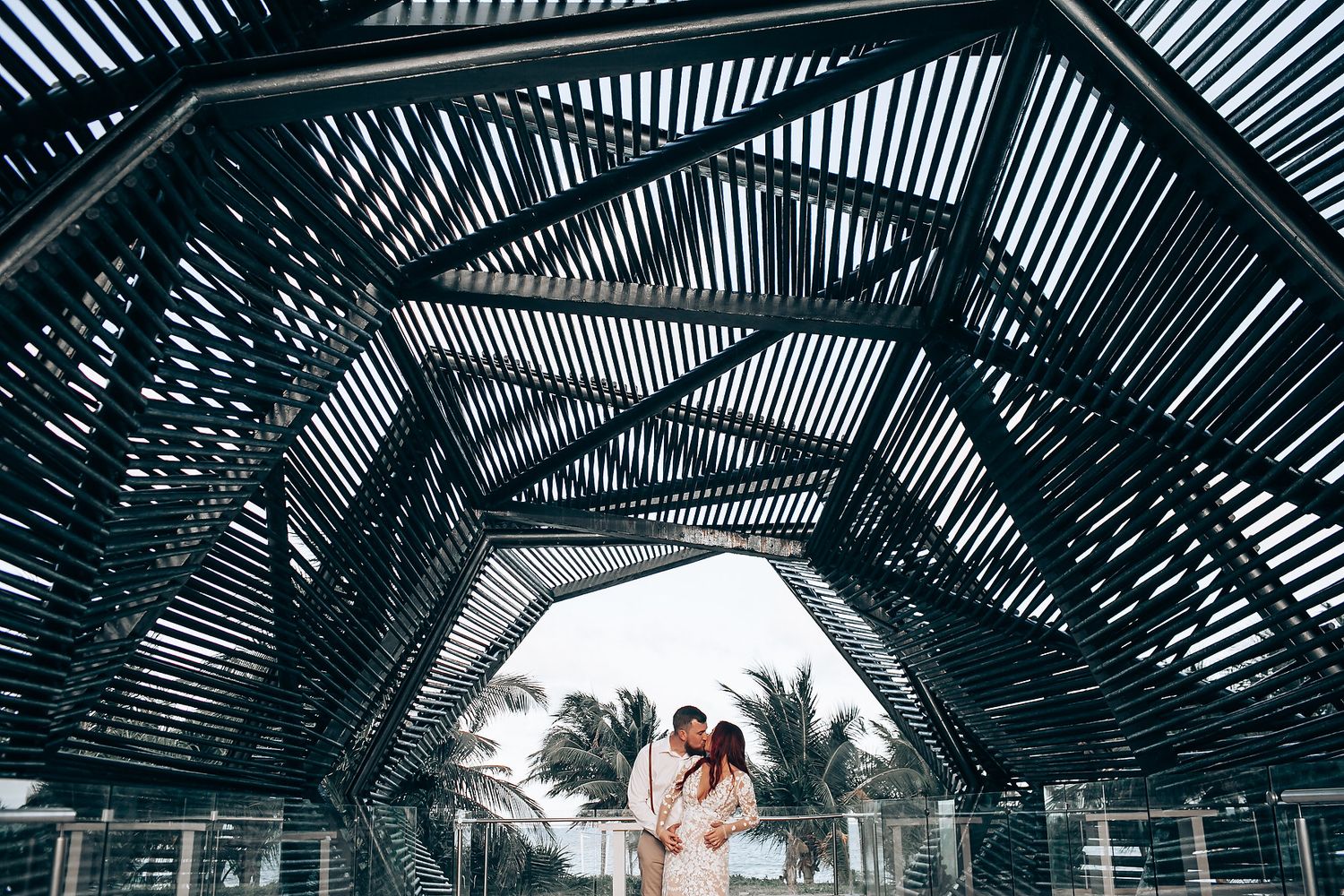 Geometric pattern of black wooden beams creating dramatic shadows and lines against bright sky through tropical palm trees.