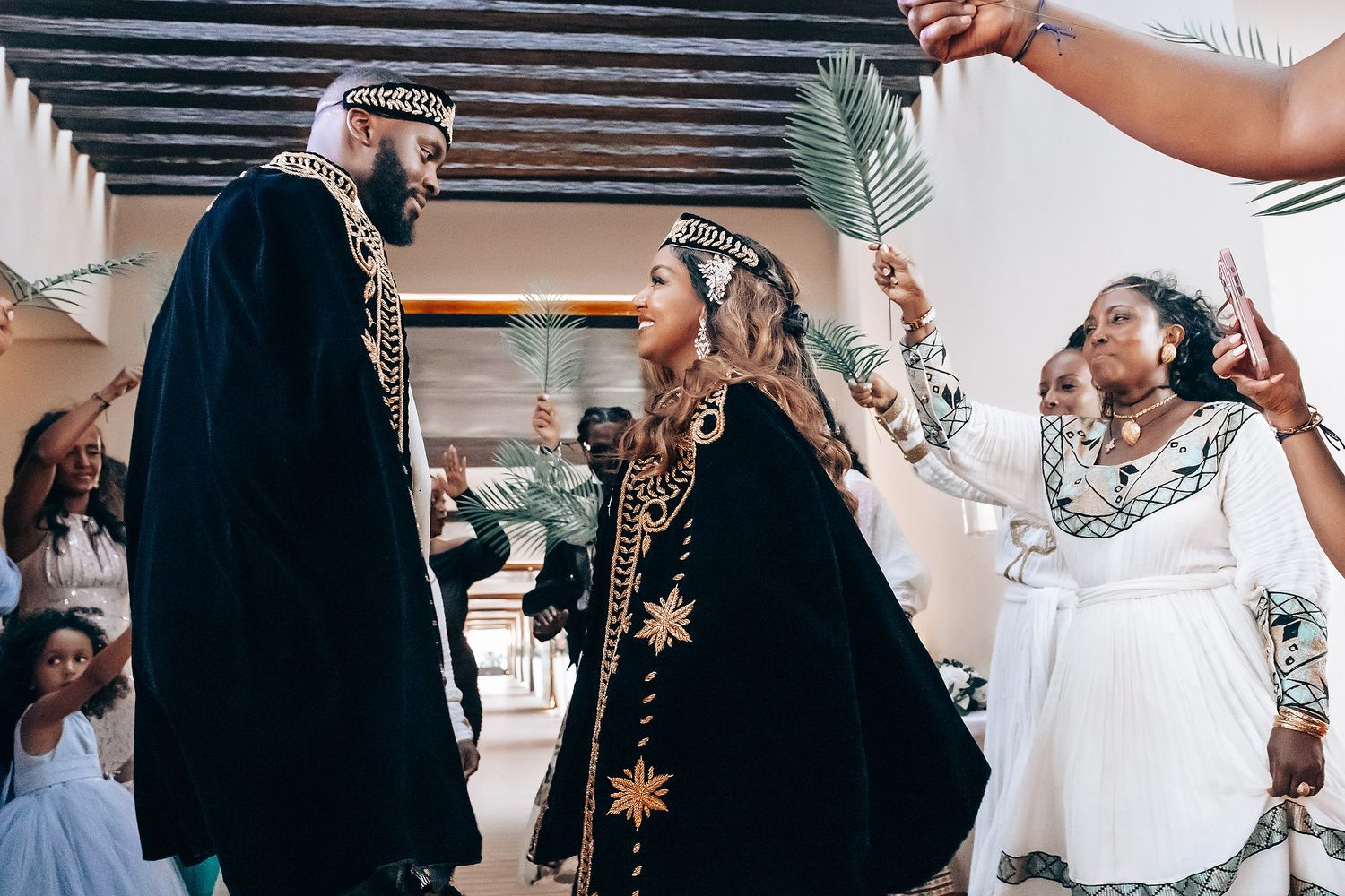 Wedding celebration with guests in ornate cultural attire raising palm fronds during ceremony.