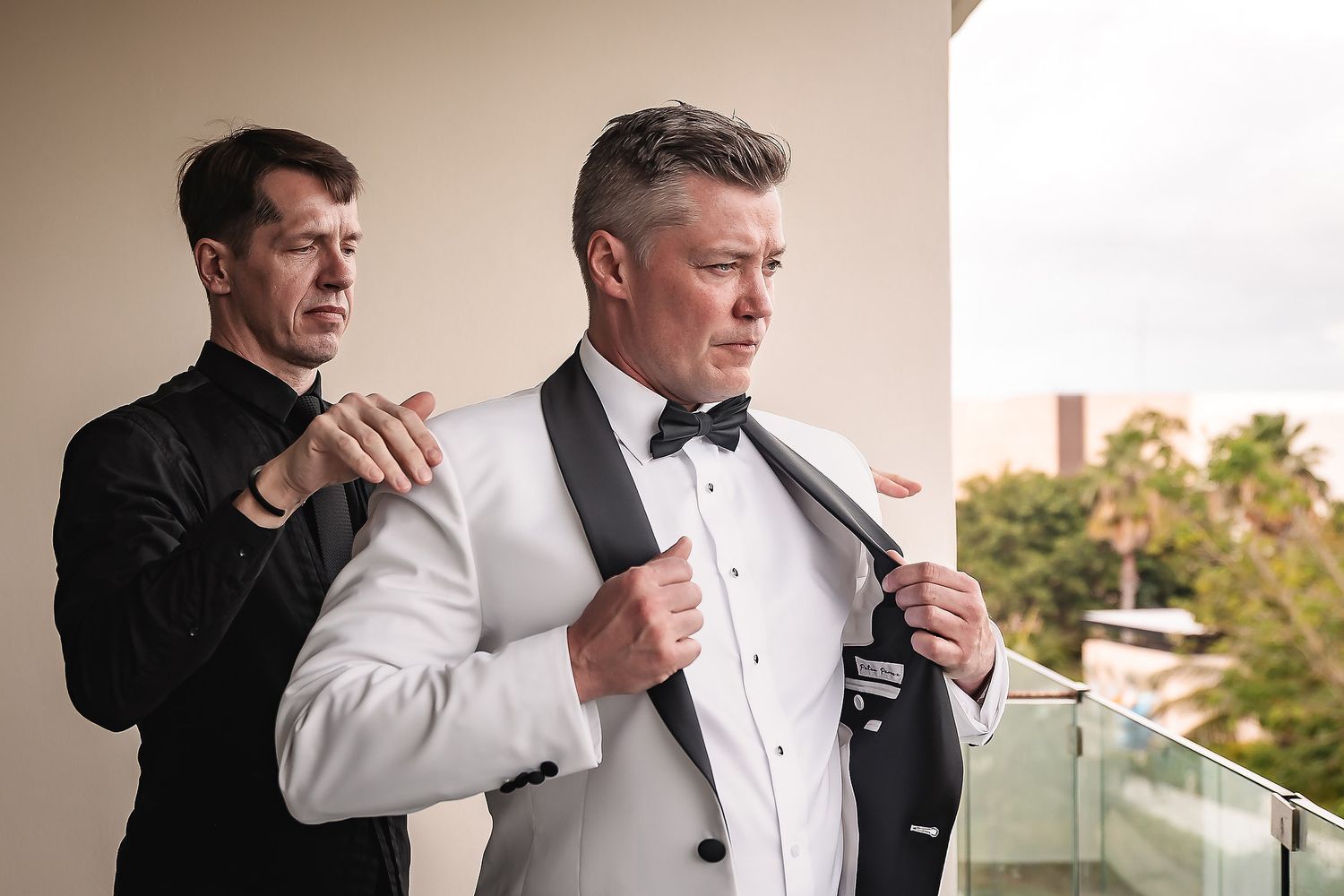 A group of groomsmen in black and white tuxedos prepare for a wedding ceremony on a sunny day.