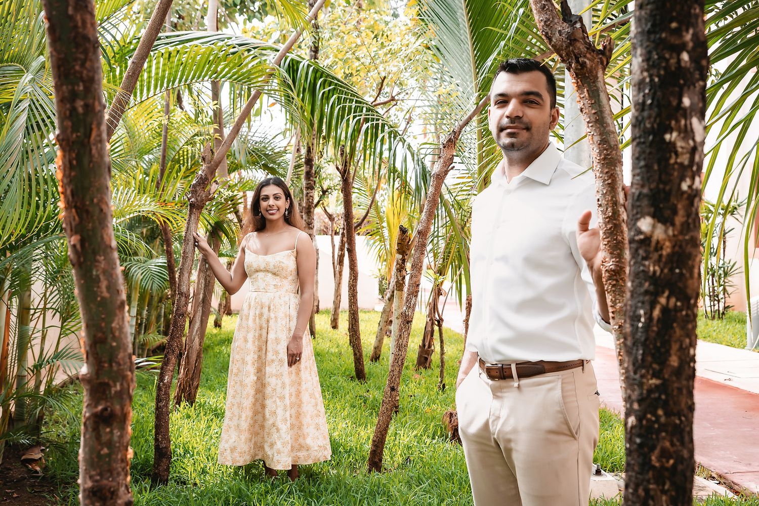 Couple strolls hand in hand along a palm-lined pathway in a tropical garden setting.