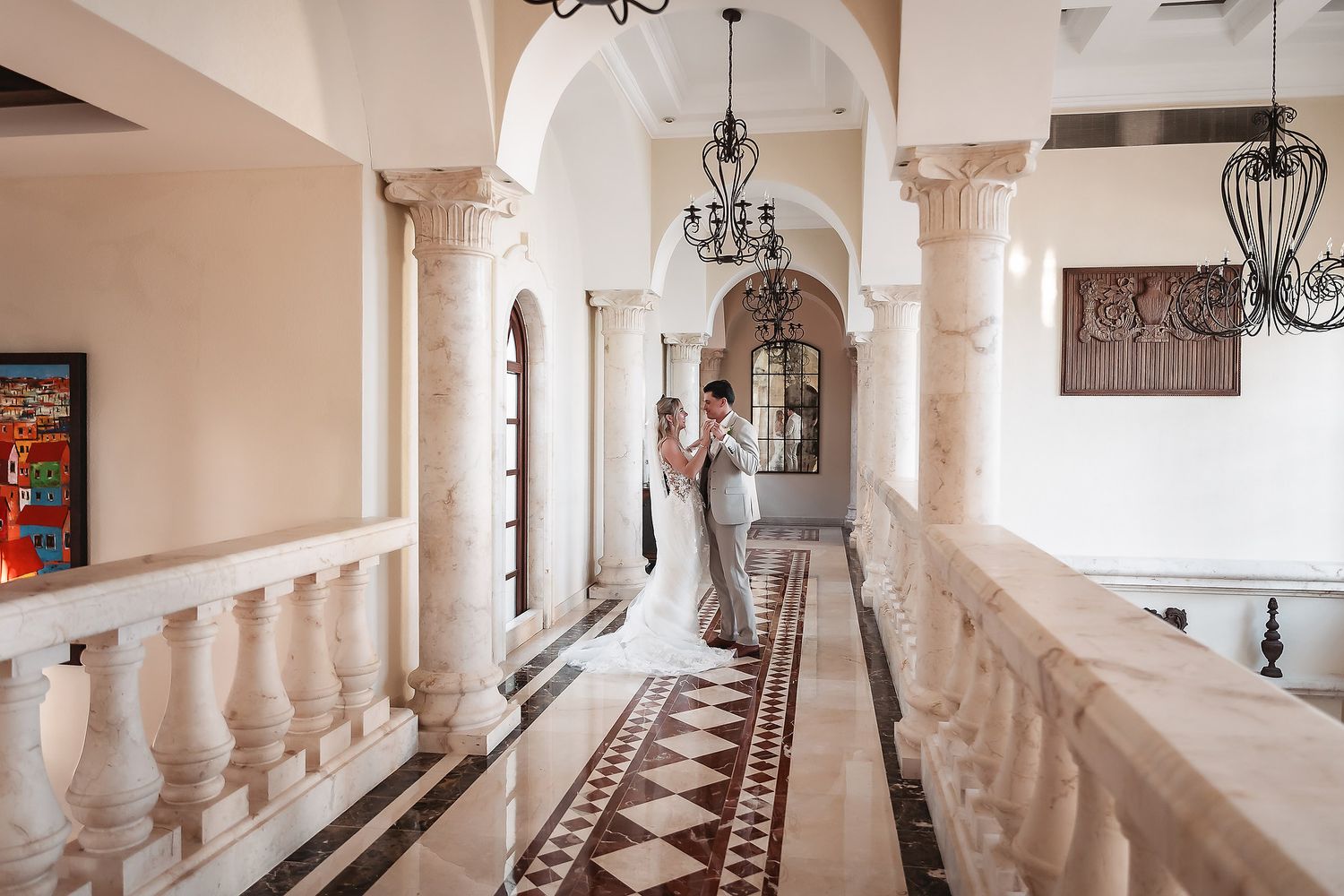 Elegant hallway features white columns, wrought iron chandeliers and patterned floor tiles.