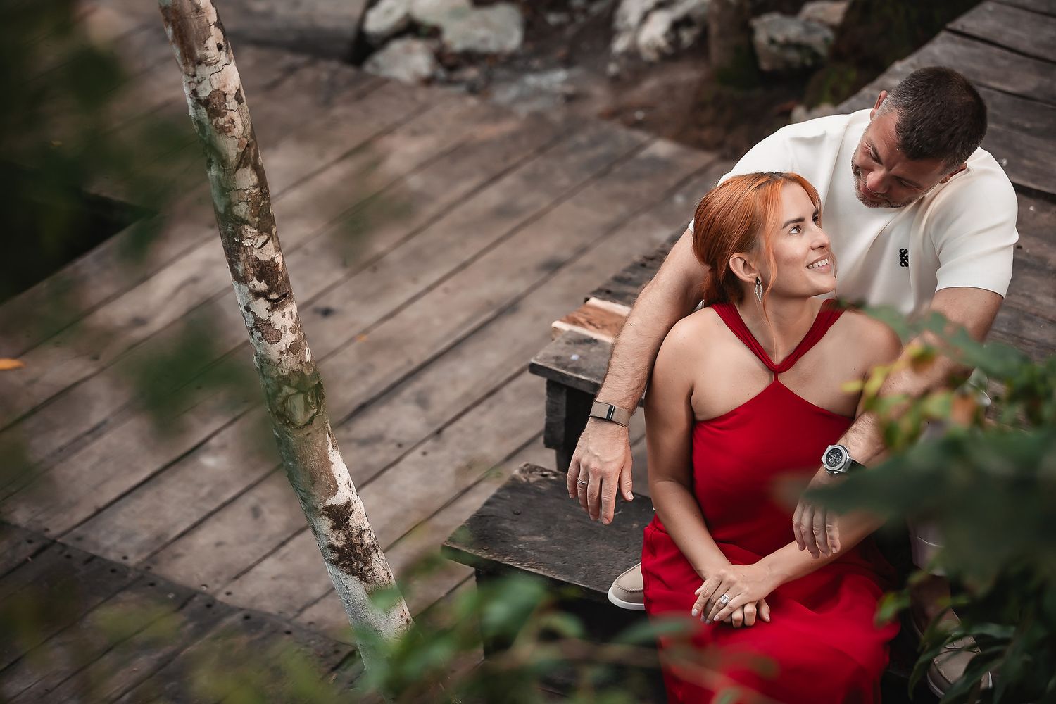 A romantic couple shares an intimate moment on a wooden deck surrounded by nature.