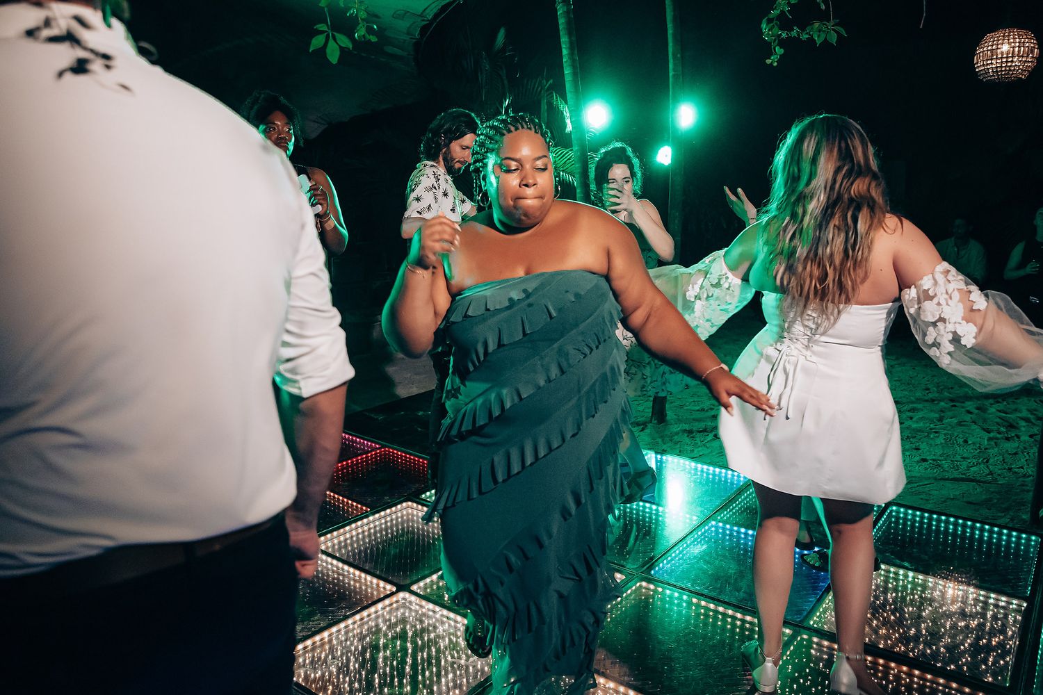 Party guests dancing on an illuminated LED dance floor at a nighttime outdoor event with green lighting.