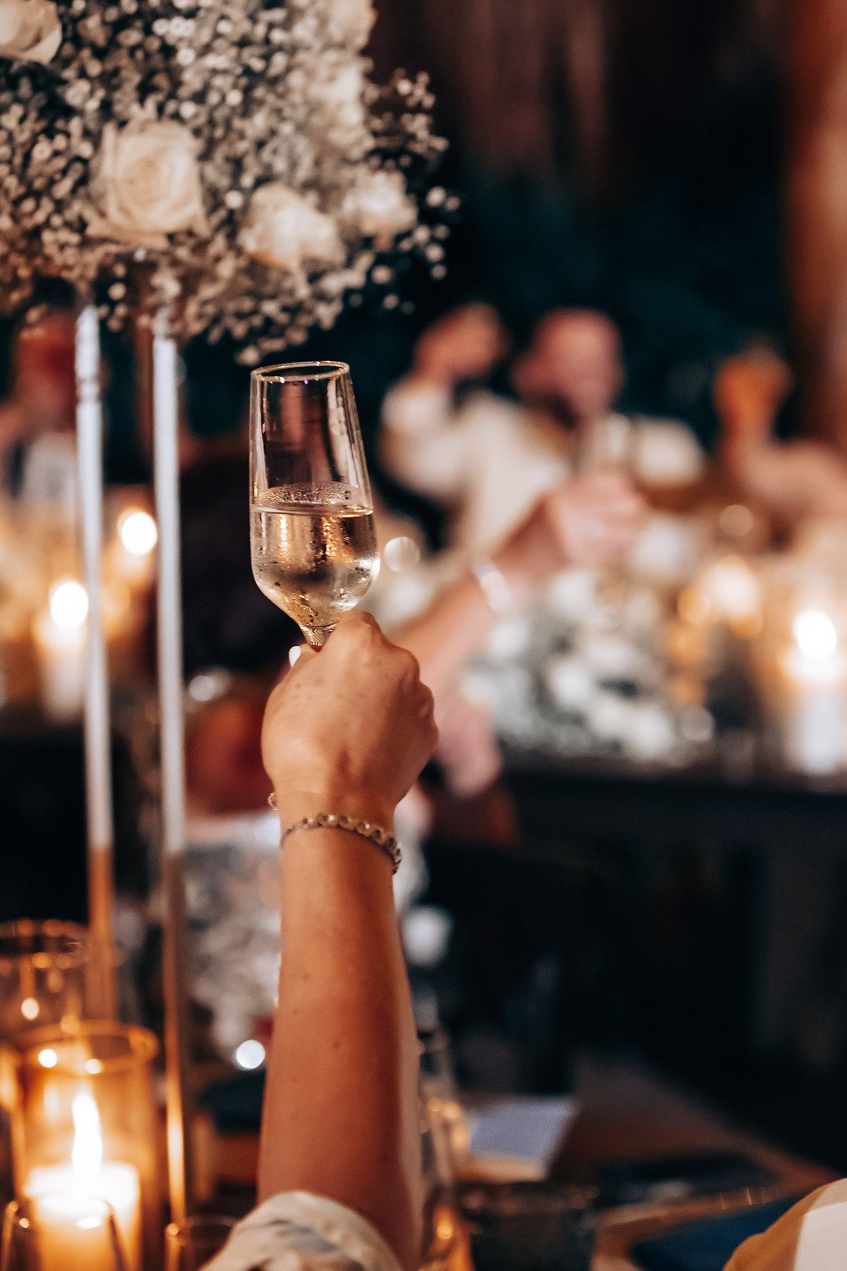 Hands raise champagne glasses for a toast at an elegant candlelit wedding reception.