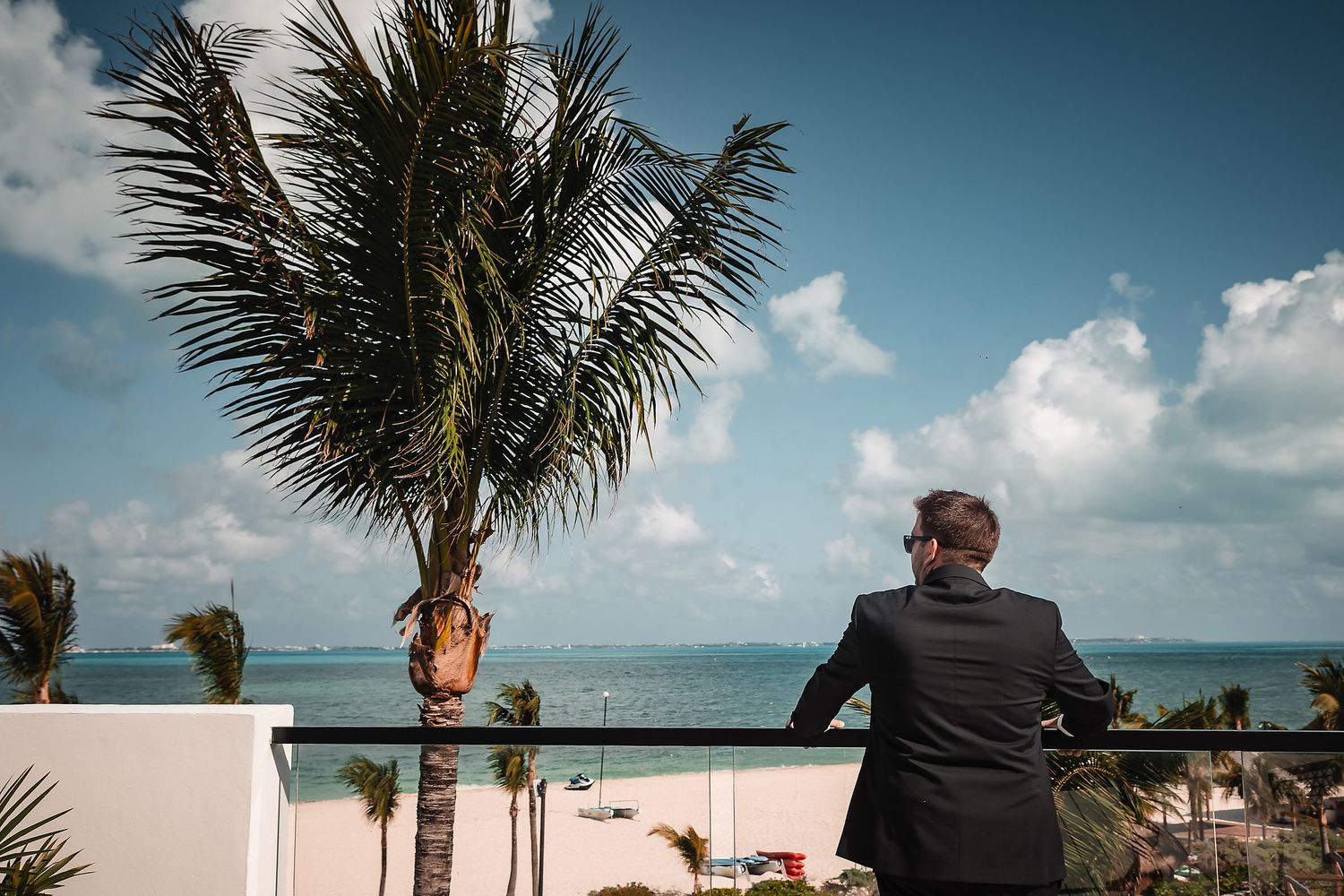 View of a tropical beach resort with palm trees and ocean from a balcony perspective.