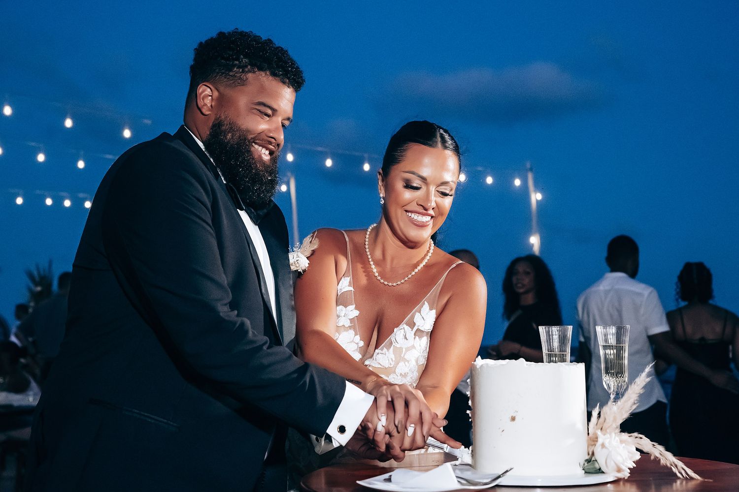 Evening wedding reception under string lights with couple sharing dessert at table.